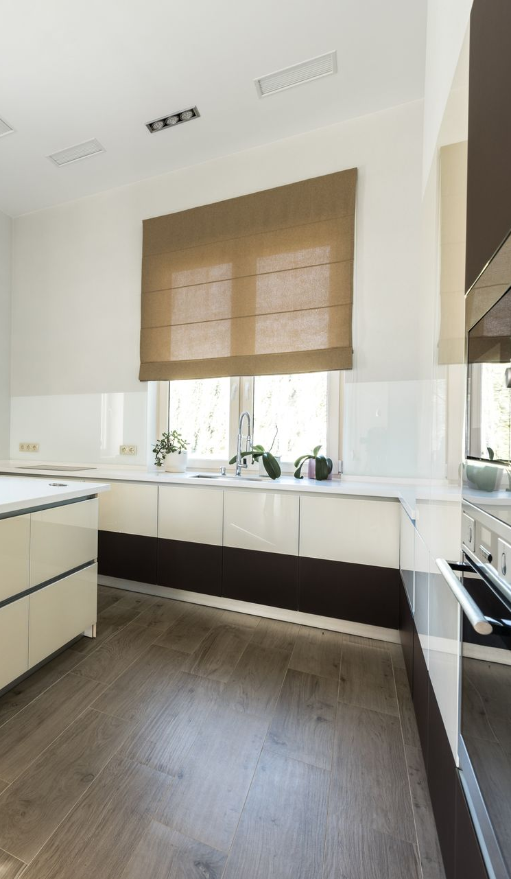 Bright modern kitchen with white cabinets, wood floor, sink under a window, and a woven blind.