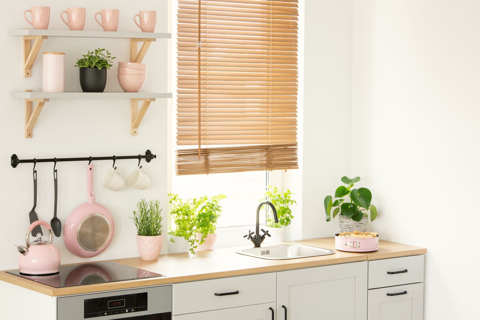 Bright kitchen with white cabinets, wooden blinds, and pink decor on shelves and countertop Bright kitchen with white cabinets, wooden blinds, and pink decor on shelves and countertop
