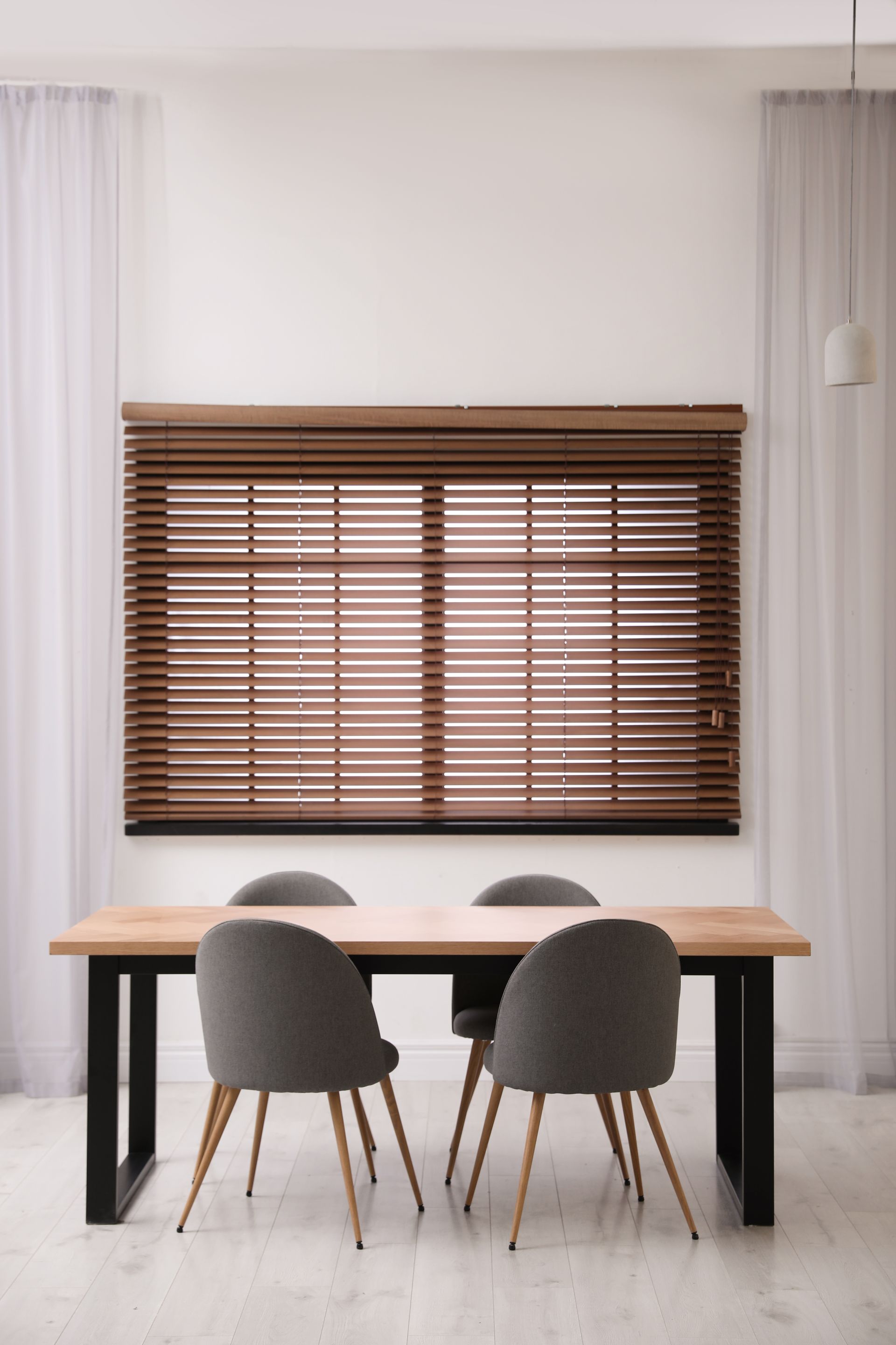 Dining table with four chairs in a bright room beneath a window with wooden blinds. Dining table with four chairs in a bright room beneath a window with wooden blinds.