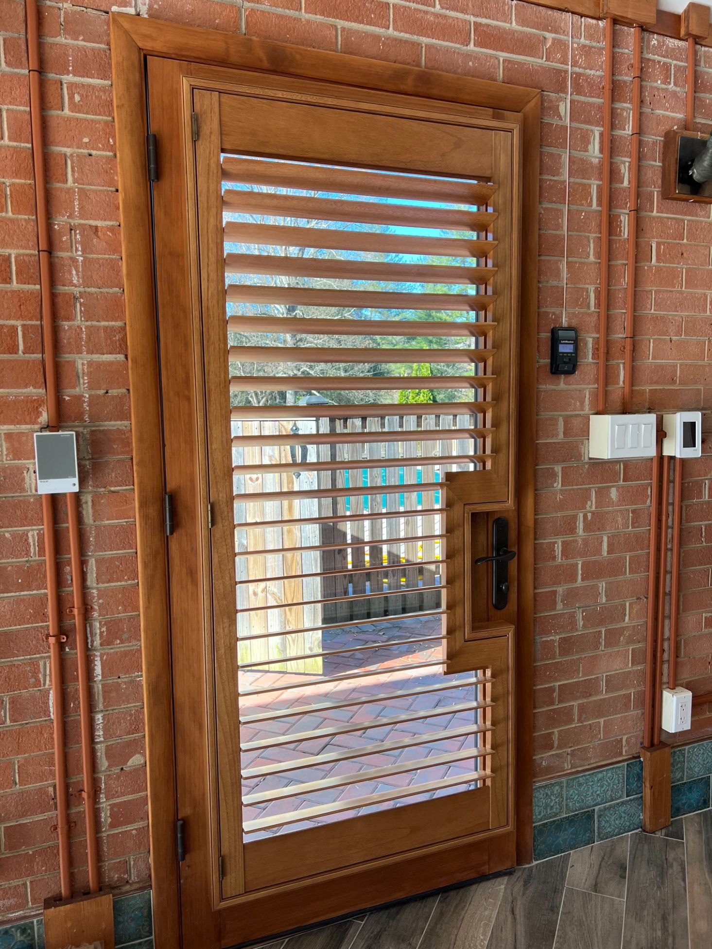 Wooden shutters on a door with glass panels set in a red brick wall, with an access keypad beside it