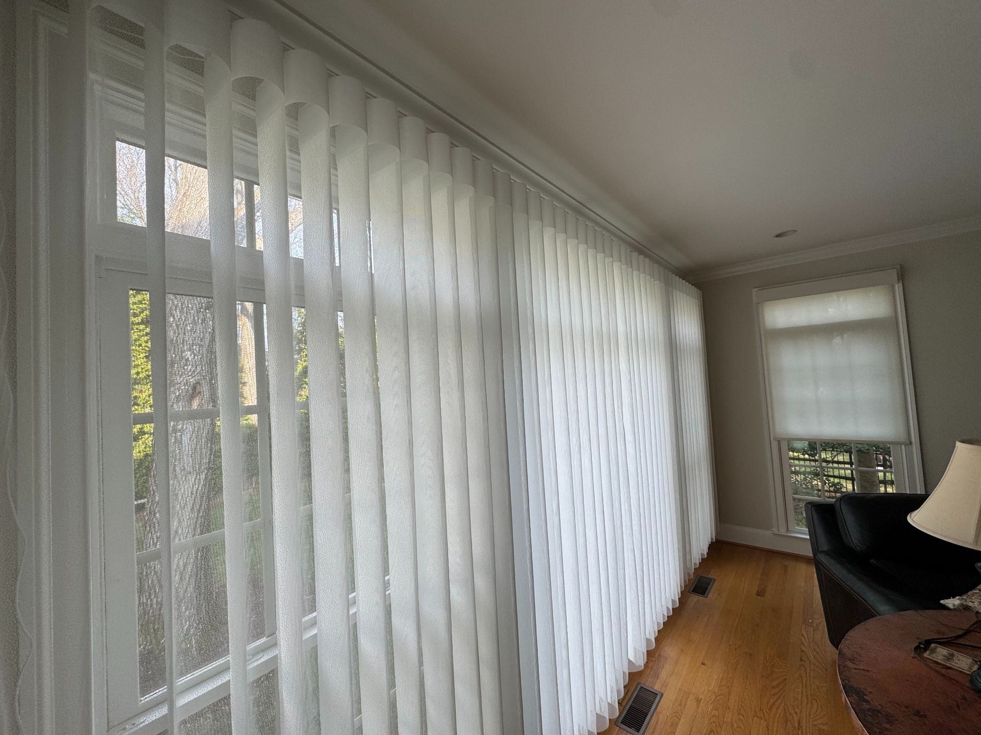 Living room with floor-to-ceiling sheer curtains, a window seat, wood floor, and a black chair by the window