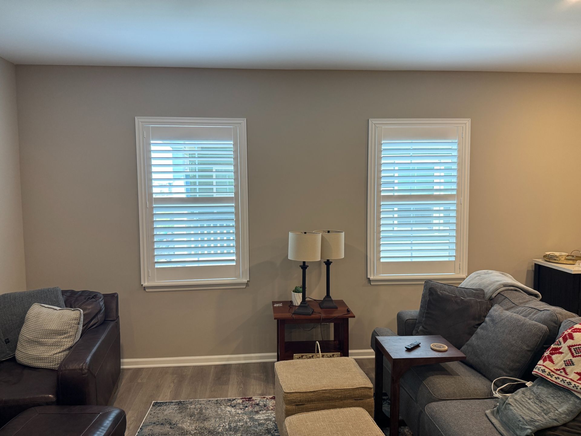 Living room with two sofas, two windows with interior shutters, a lamp, and a patterned rug