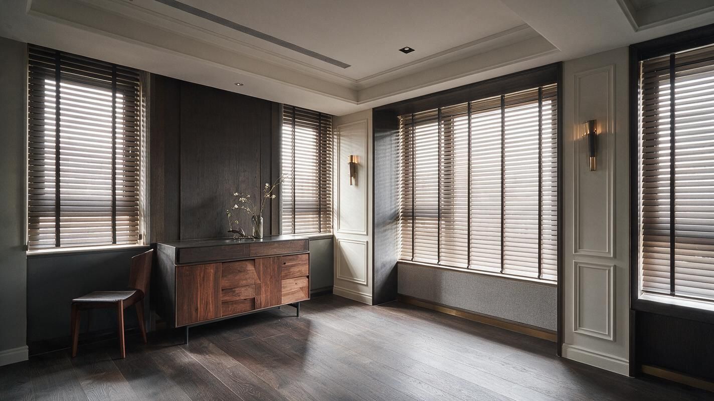 Modern living room with large windows, dark blinds, wood cabinet, and neutral gray walls
