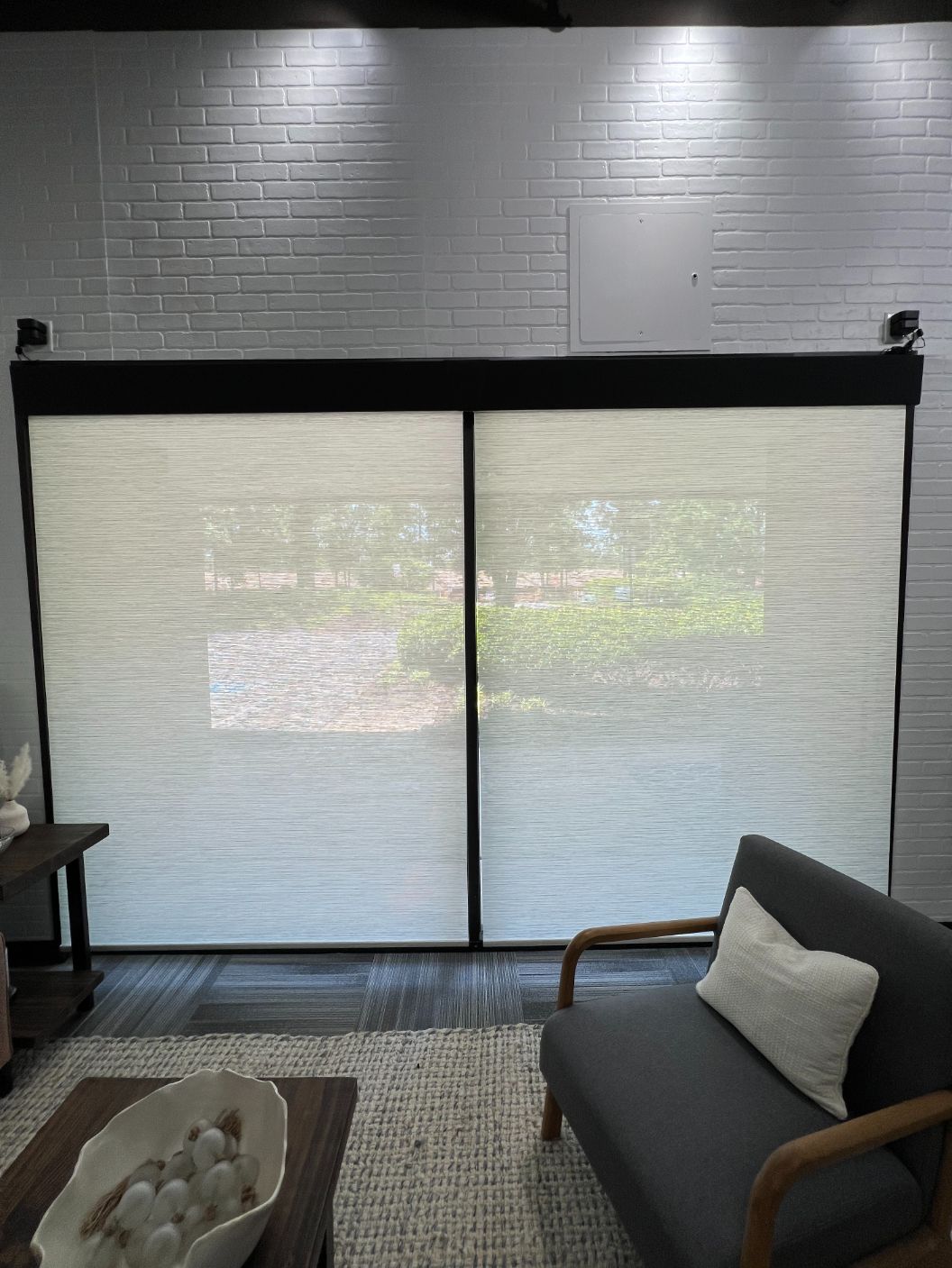 Large sliding glass door with a beige solar shade, gray couch, and rug in a modern living room.