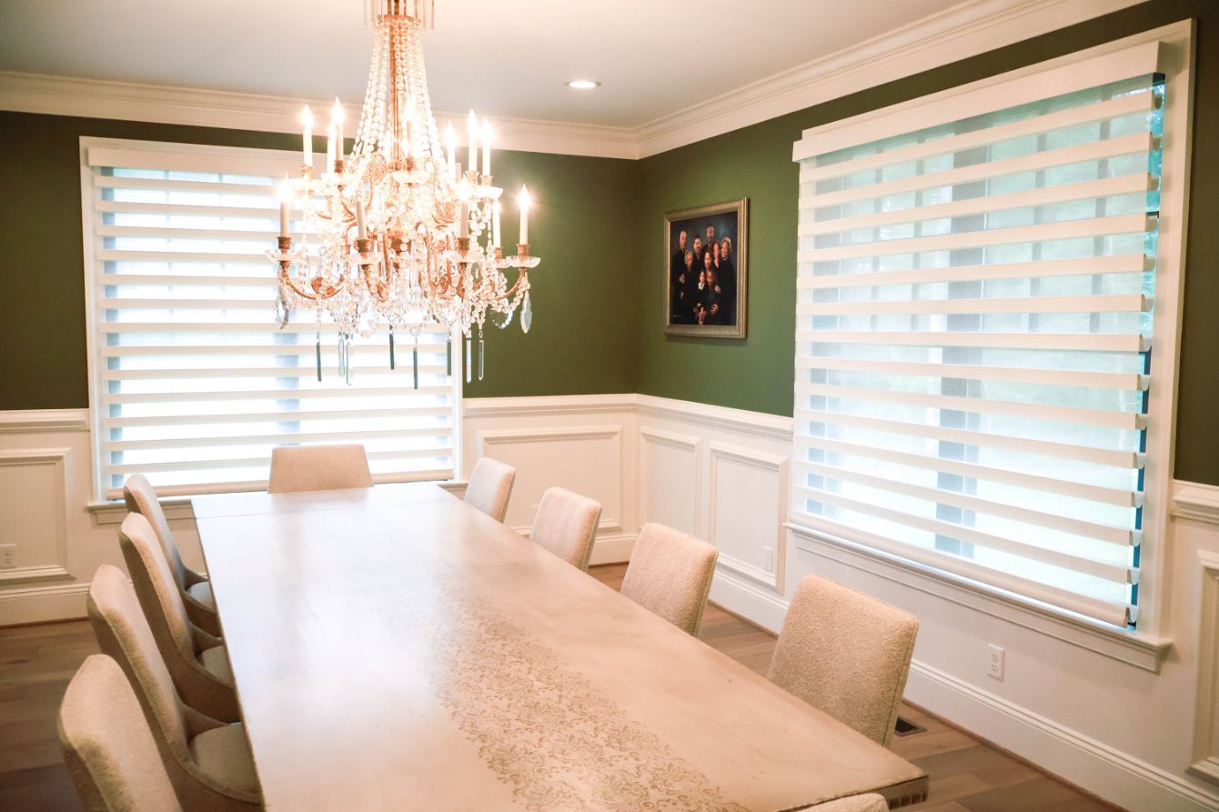 Elegant dining room with chandelier, long table, beige chairs, and motorized dual shades on the windows.