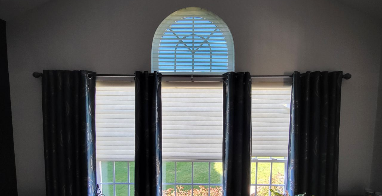Window with black curtains and white blinds under a small arched transom window