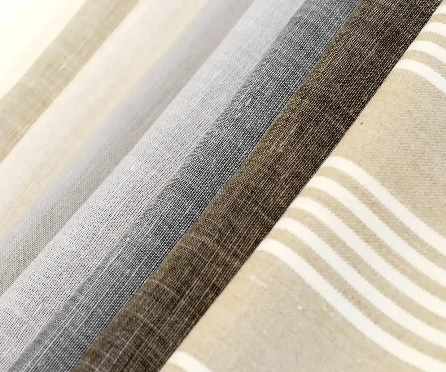 Folded textured fabrics in beige, gray, and brown with subtle striped patterns Folded textured fabrics in beige, gray, and brown with subtle striped patterns