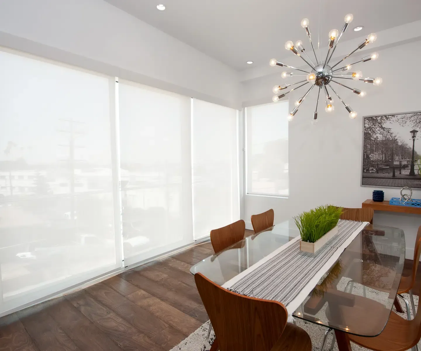 Modern dining room with glass table, wood chairs, large windows, and a starburst chandelier