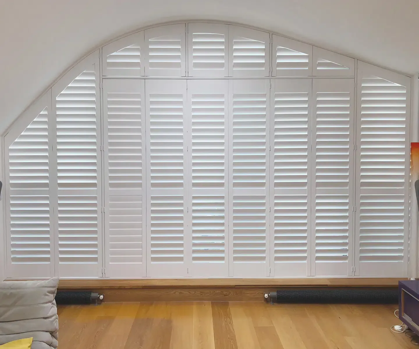 White shuttered window in an arched wall above a wooden floor, with a radiator below. White shuttered window in an arched wall above a wooden floor, with a radiator below.