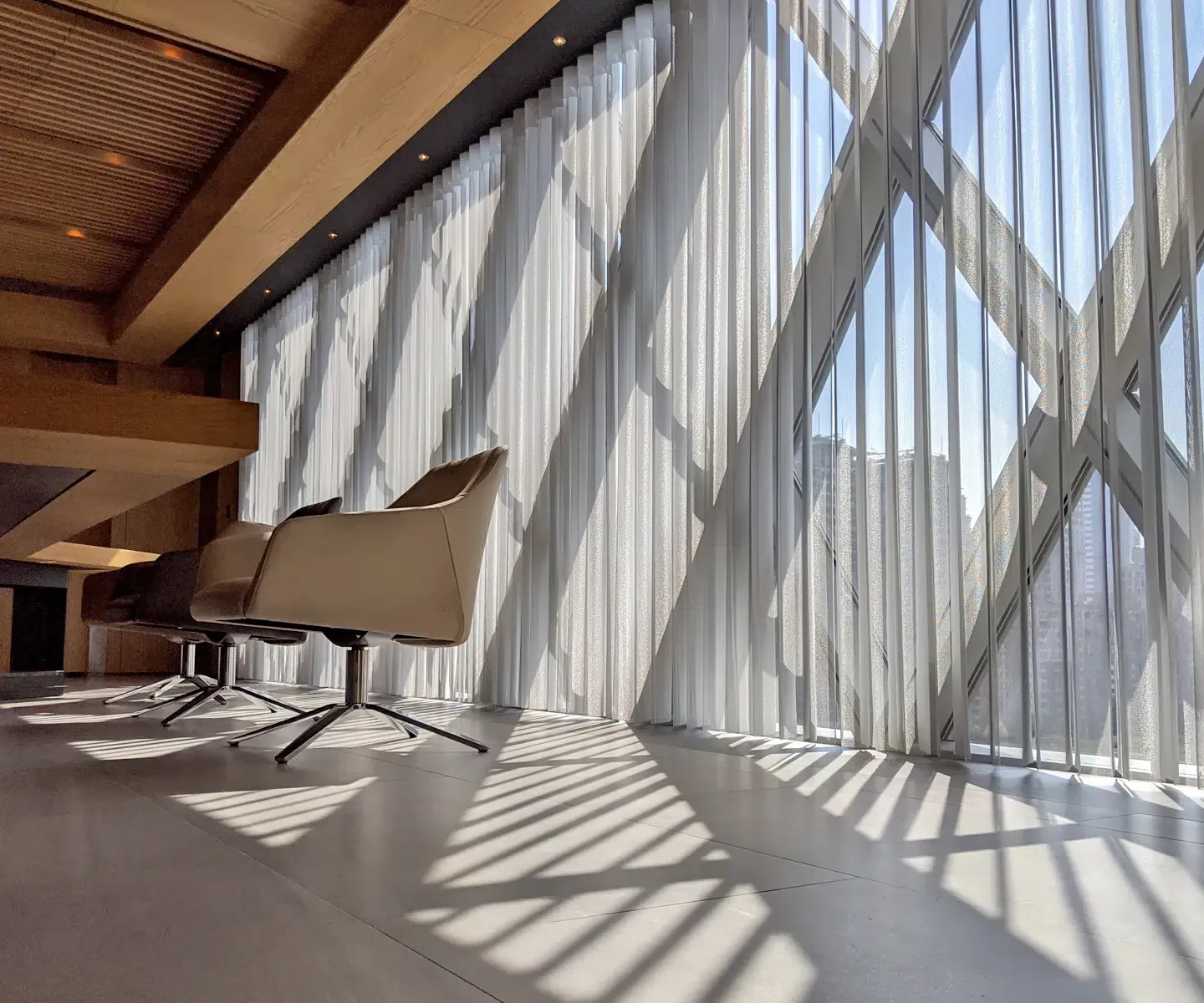 Bright modern lobby with large diagonal window shadows and a row of white lounge chairs