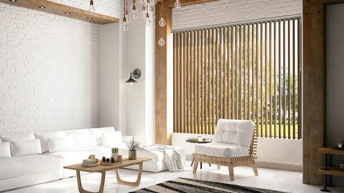 Bright modern living room with white sofa, wooden tables, chair, and large slatted window.