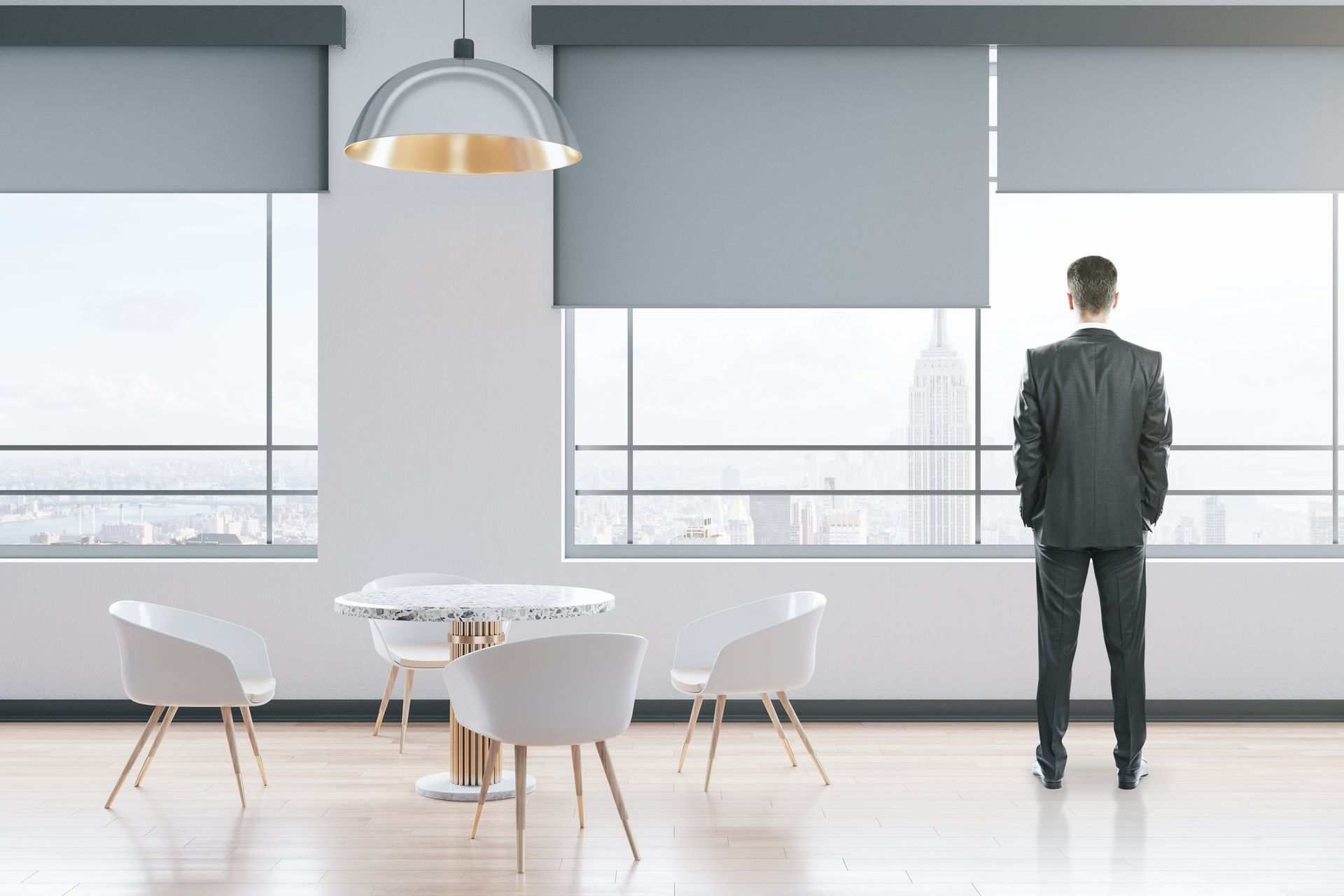 Person standing in a bright modern office, looking out large windows beside a round table and chairs