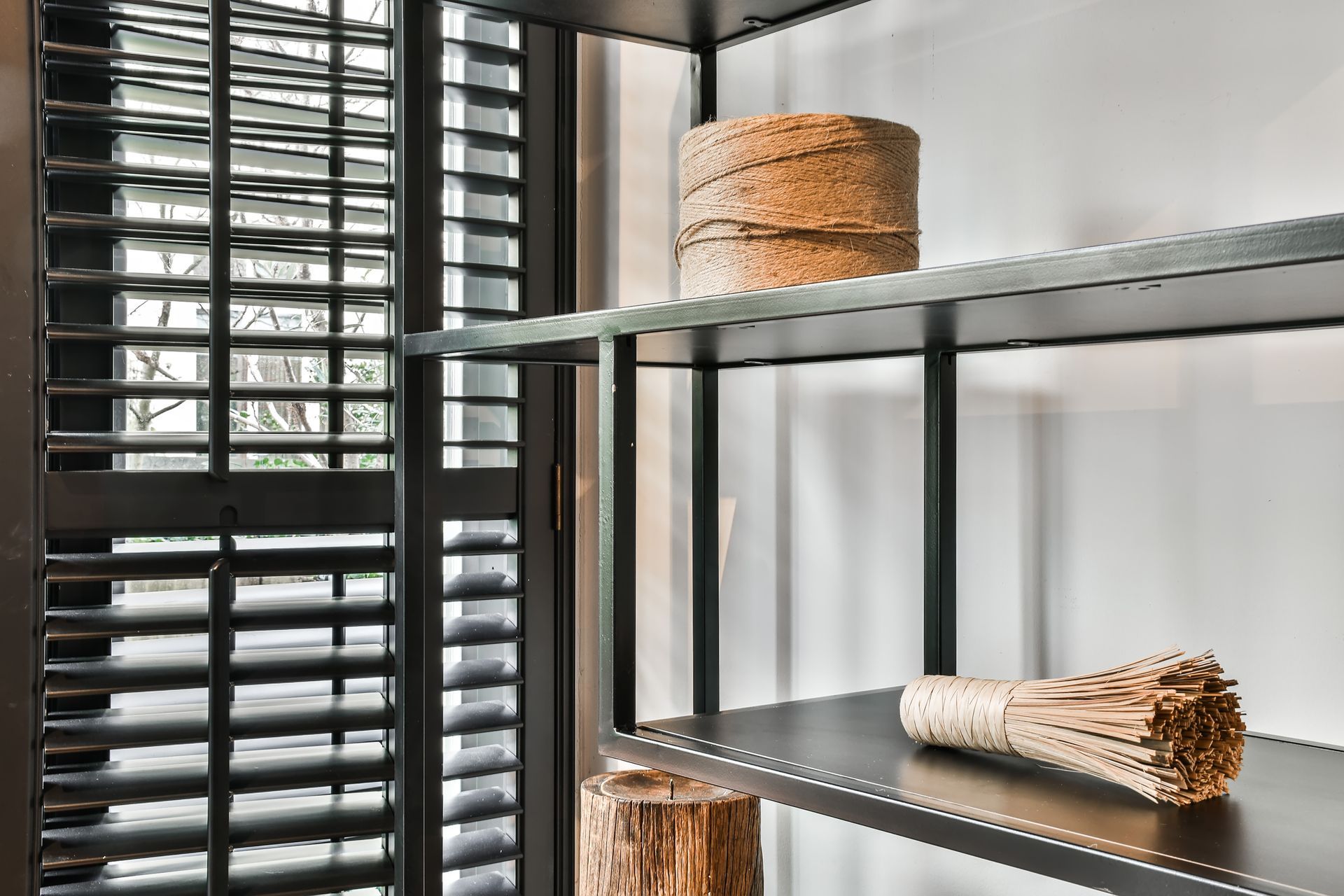 Metal shelving by a window with woven baskets and a broom in a bright room Metal shelving by a window with woven baskets and a broom in a bright room