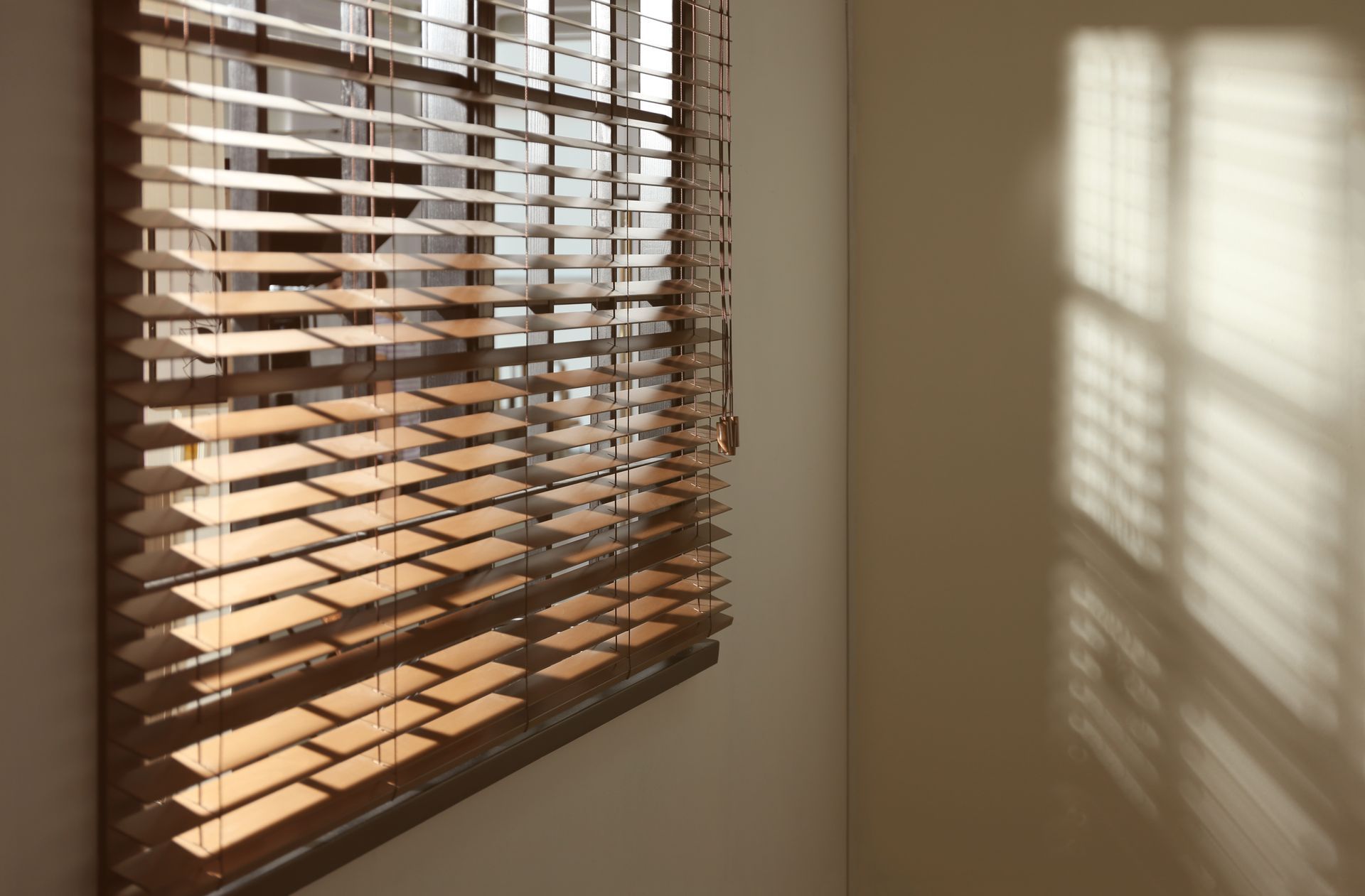 Sunlight through wooden blinds casts striped shadows on a beige wall.