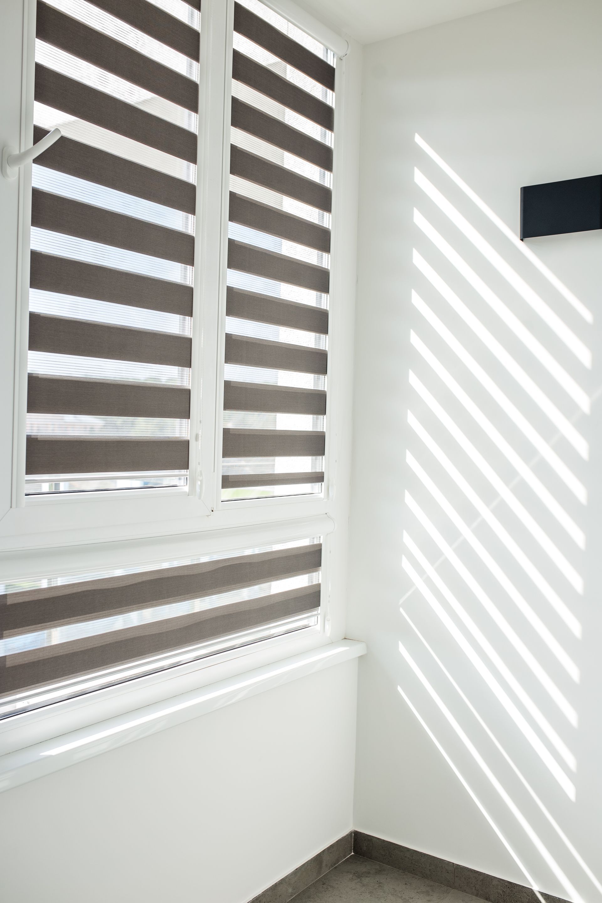 White blinds with sunlight casting striped shadows on a white wall and window ledge. White blinds with sunlight casting striped shadows on a white wall and window ledge.