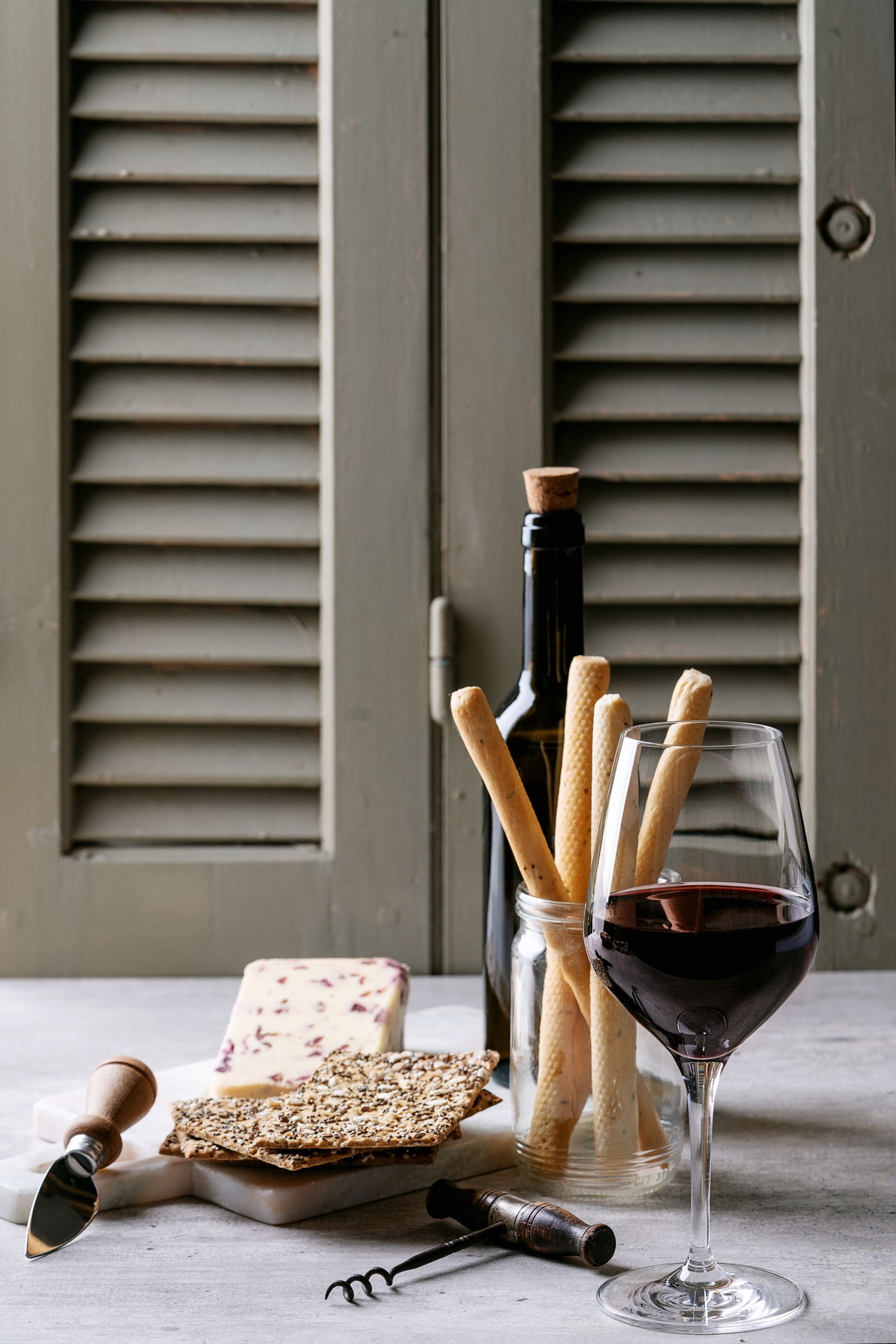 Wine glass, breadsticks, cheese, and a bottle on a rustic table by gray shutters. Wine glass, breadsticks, cheese, and a bottle on a rustic table by gray shutters.