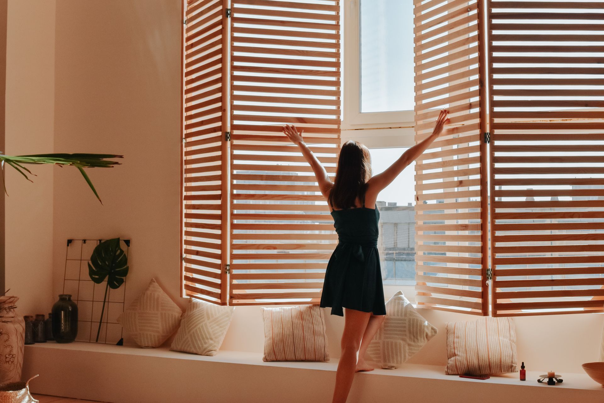 Person stretching by a sunlit window with wooden blinds in a cozy living room Person stretching by a sunlit window with wooden blinds in a cozy living room
