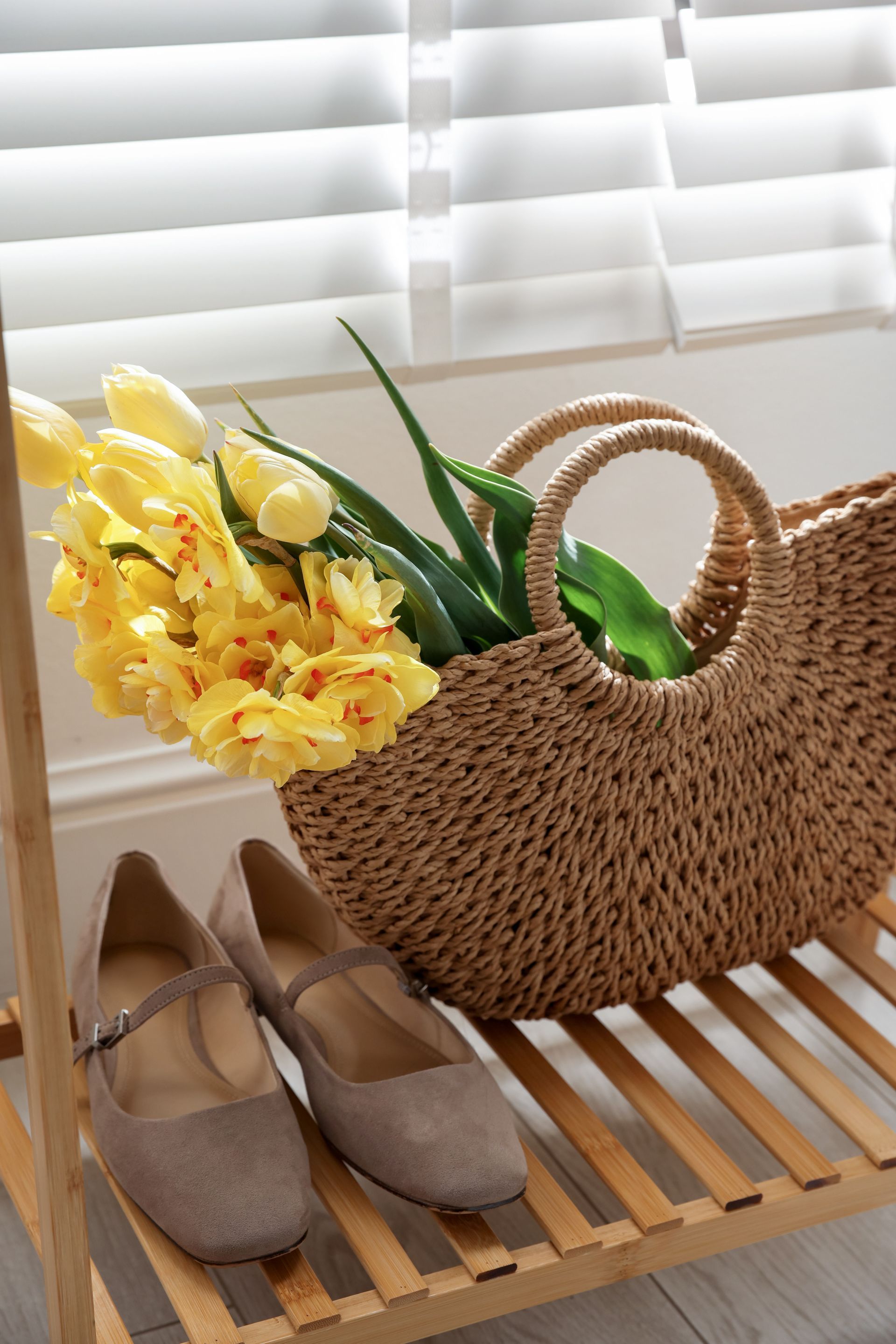 Woven basket with yellow flowers and green leaves beside beige flats on a slatted bench Woven basket with yellow flowers and green leaves beside beige flats on a slatted bench