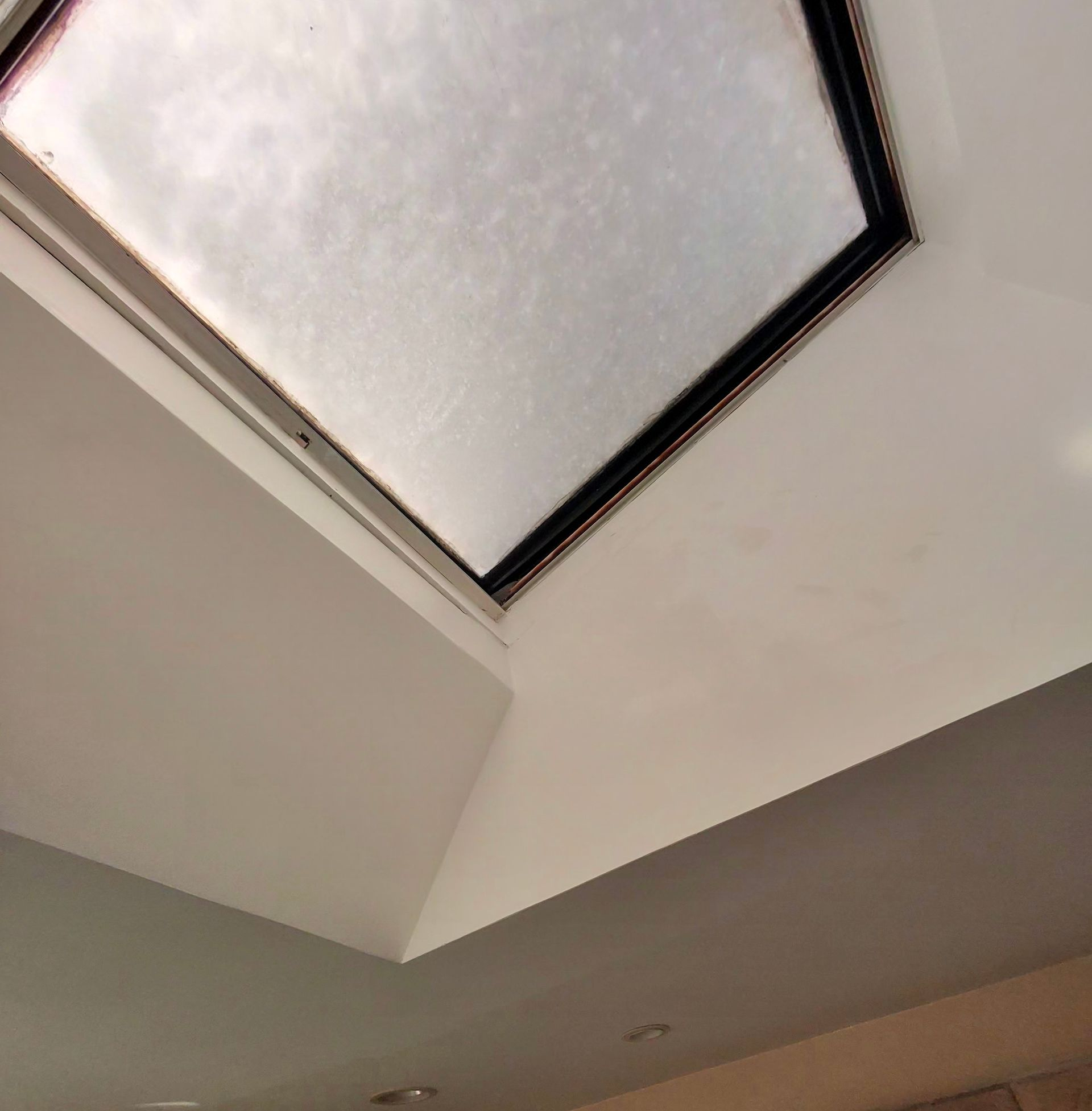 A square skylight set into a white, angled ceiling with visible moisture or light staining along the frame.
