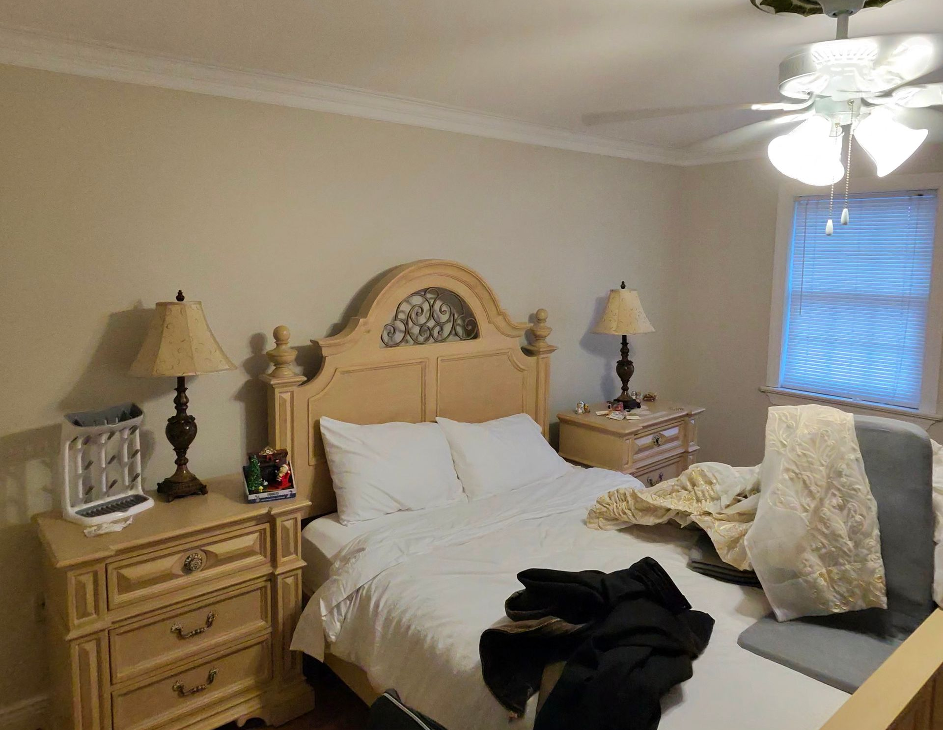 A bedroom featuring a bed with a light-colored wooden headboard, two matching nightstands, lamps, and a ceiling fan.