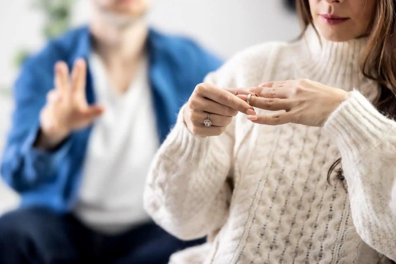 Una donna si toglie un anello, mentre un uomo sullo sfondo fa gesti con le mani, suggerendo una rottura.