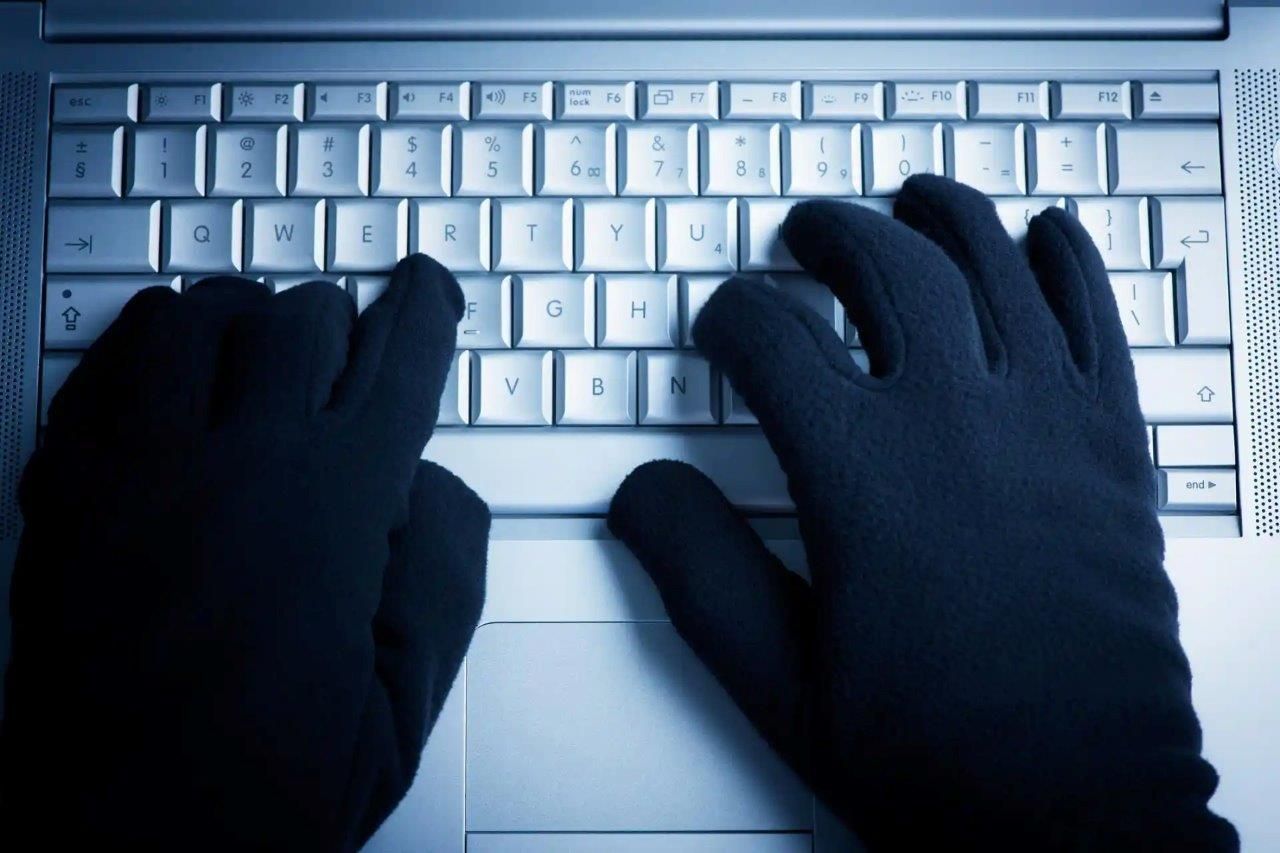 Mani in guanti neri che digitano sulla tastiera di un computer.