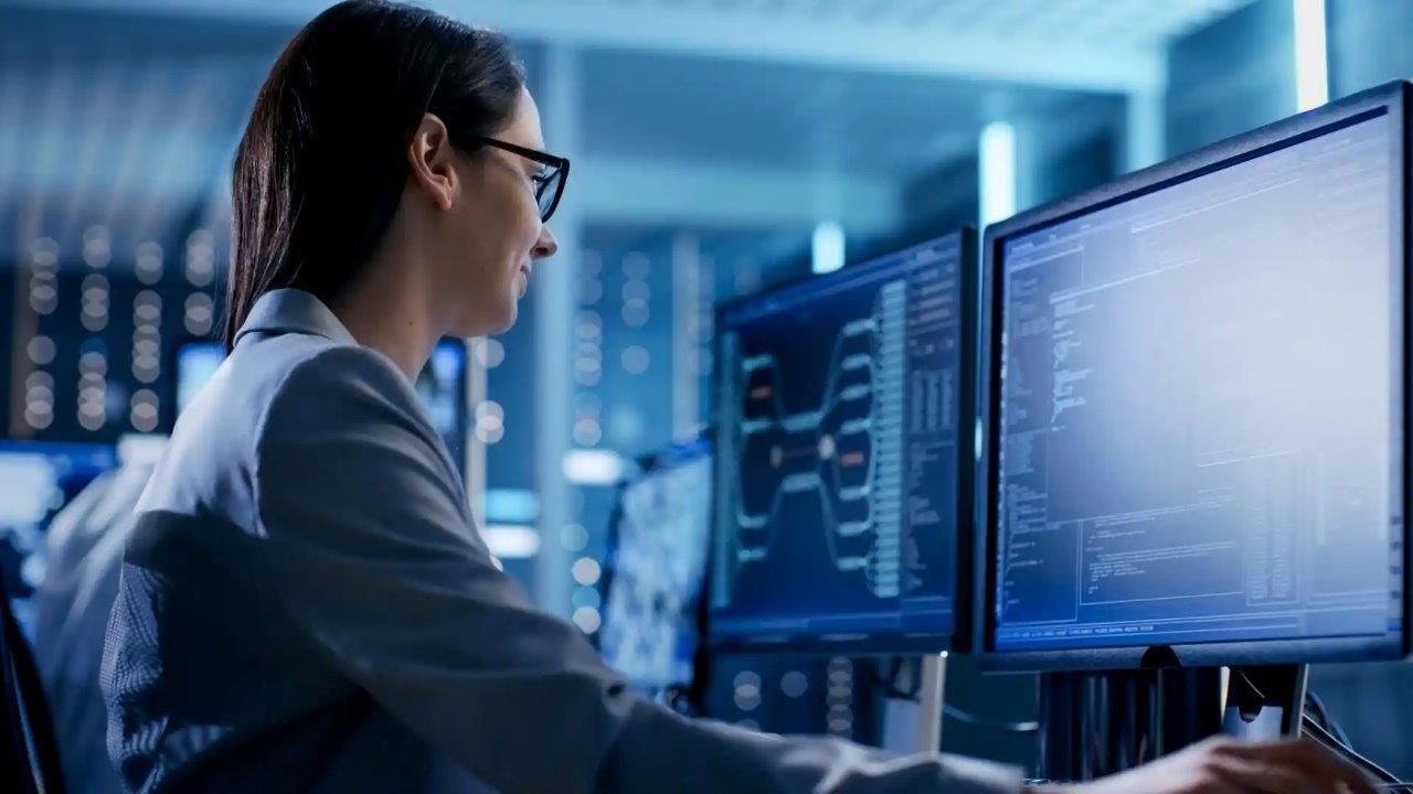 Donna con gli occhiali che lavora ai monitor dei computer in una sala server.