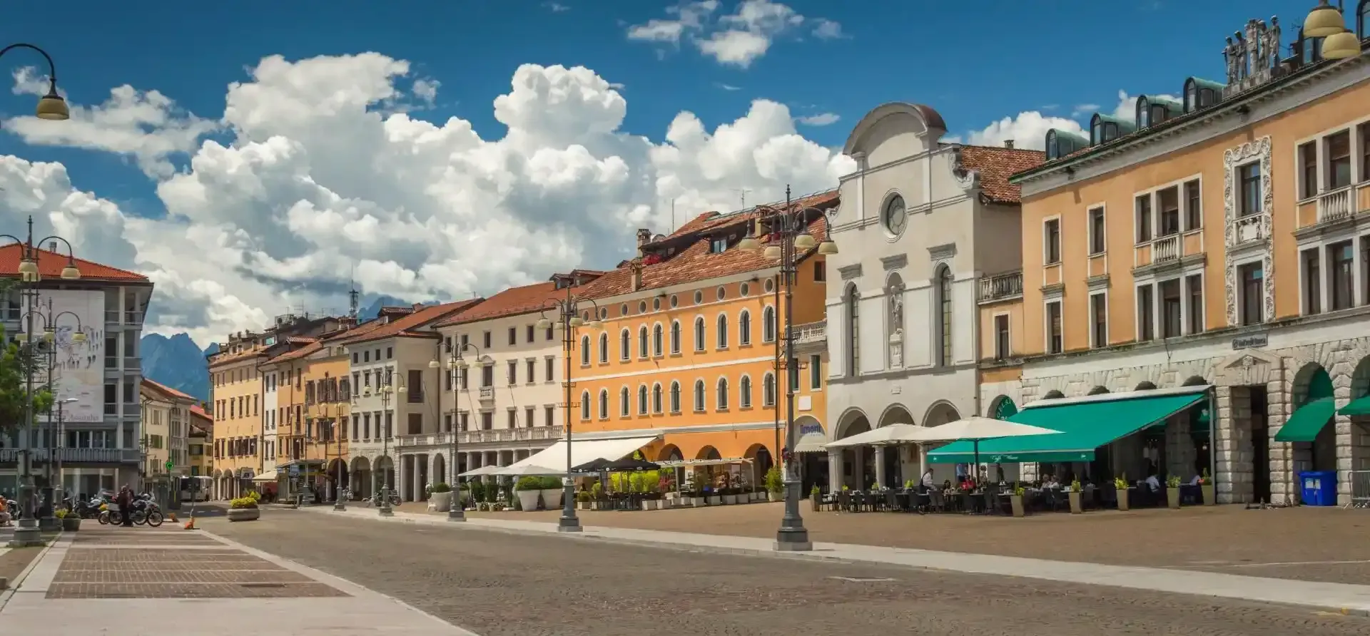 Edifici fiancheggiano piazza acciottolata, il cielo è azzurro con qualche nuvola.