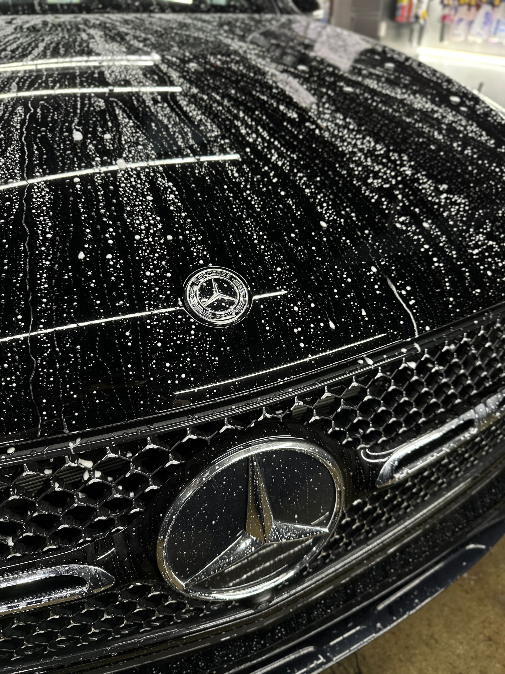 Close-up of a black Mercedes-Benz hood and grille covered in water droplets.