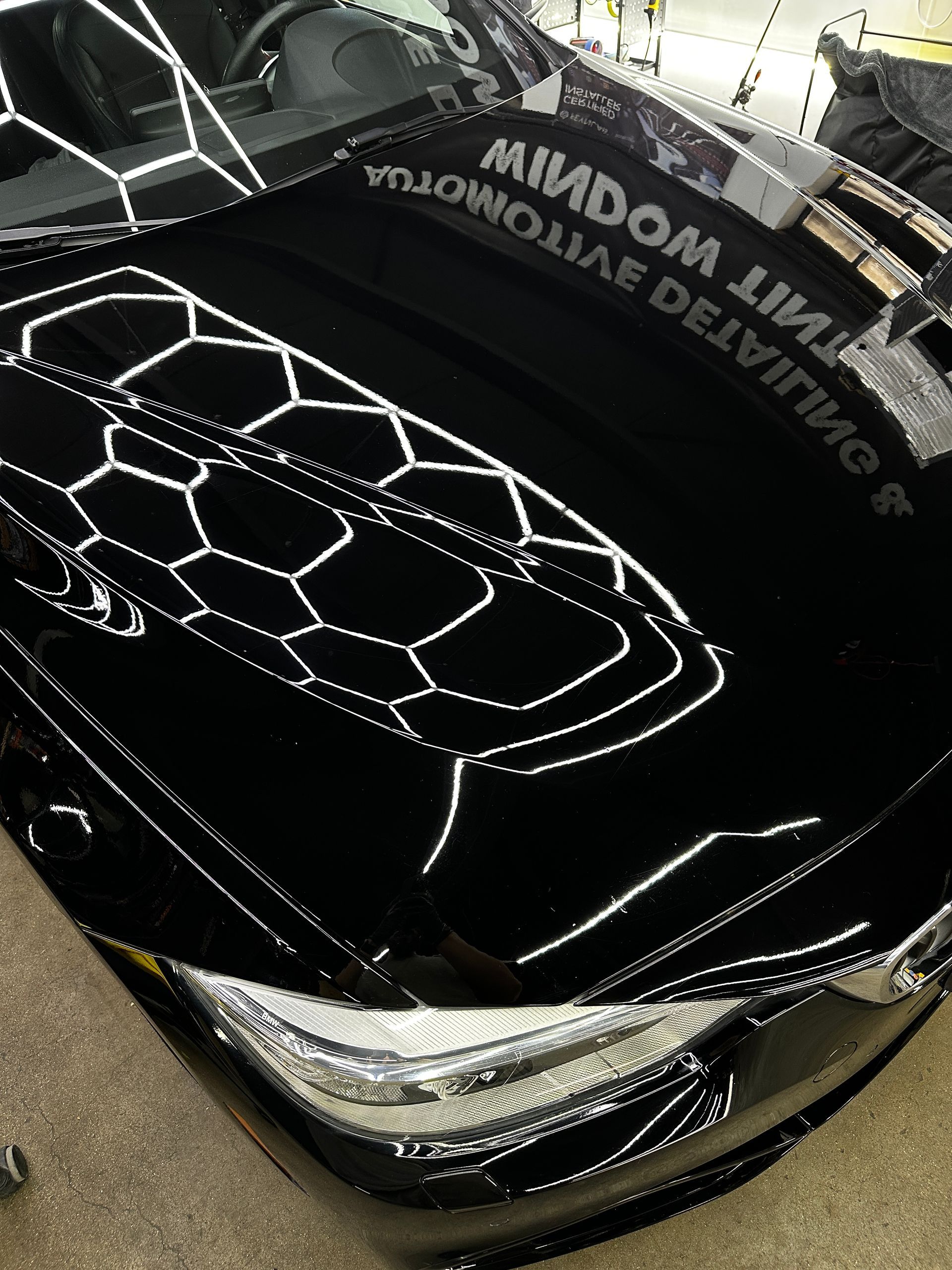 Reflections of shop lighting and a company sign on the polished, black hood of a car.