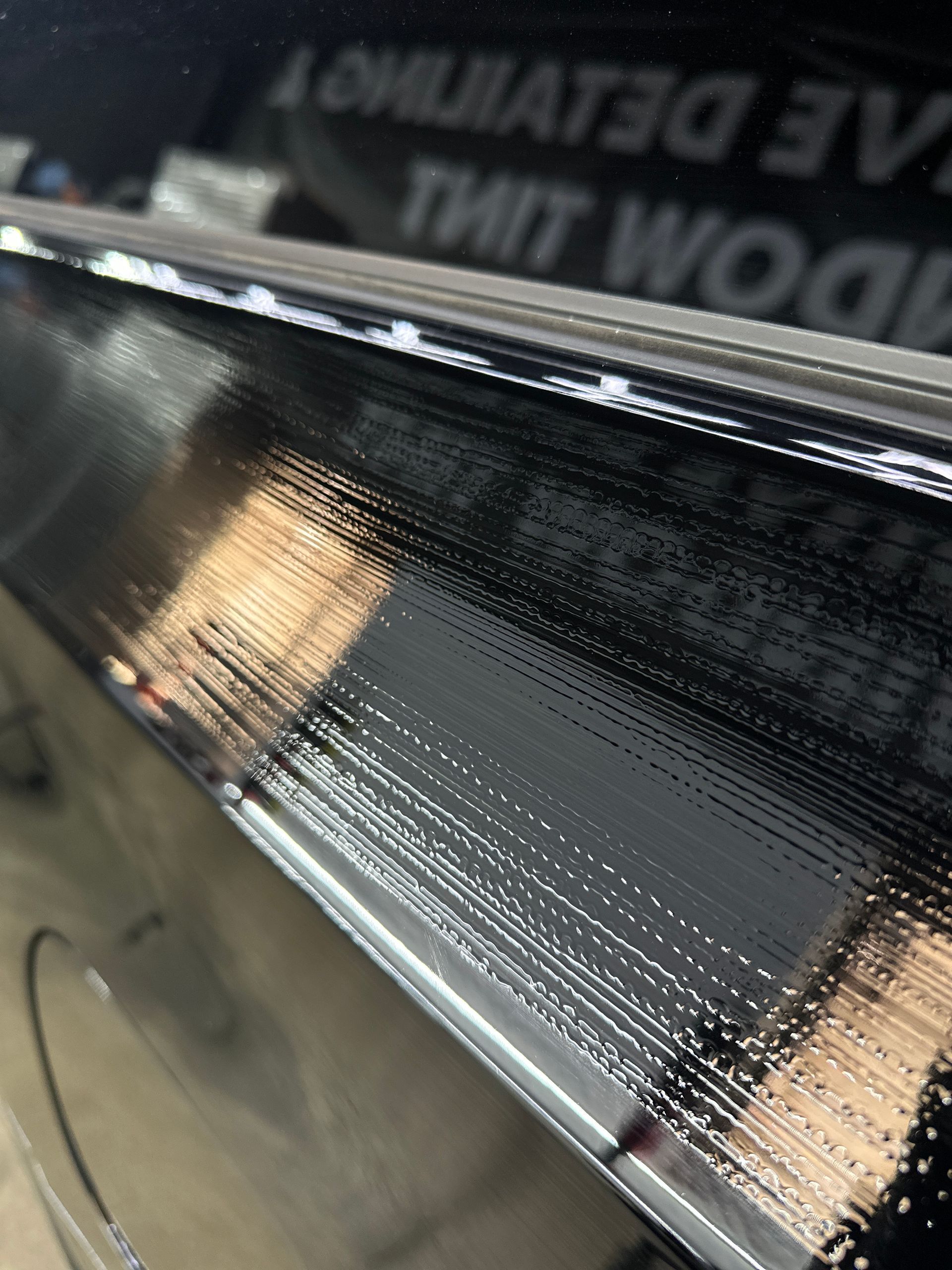 A close-up view of a car's black window trim showing significant surface scratches and swirl marks under bright lighting.