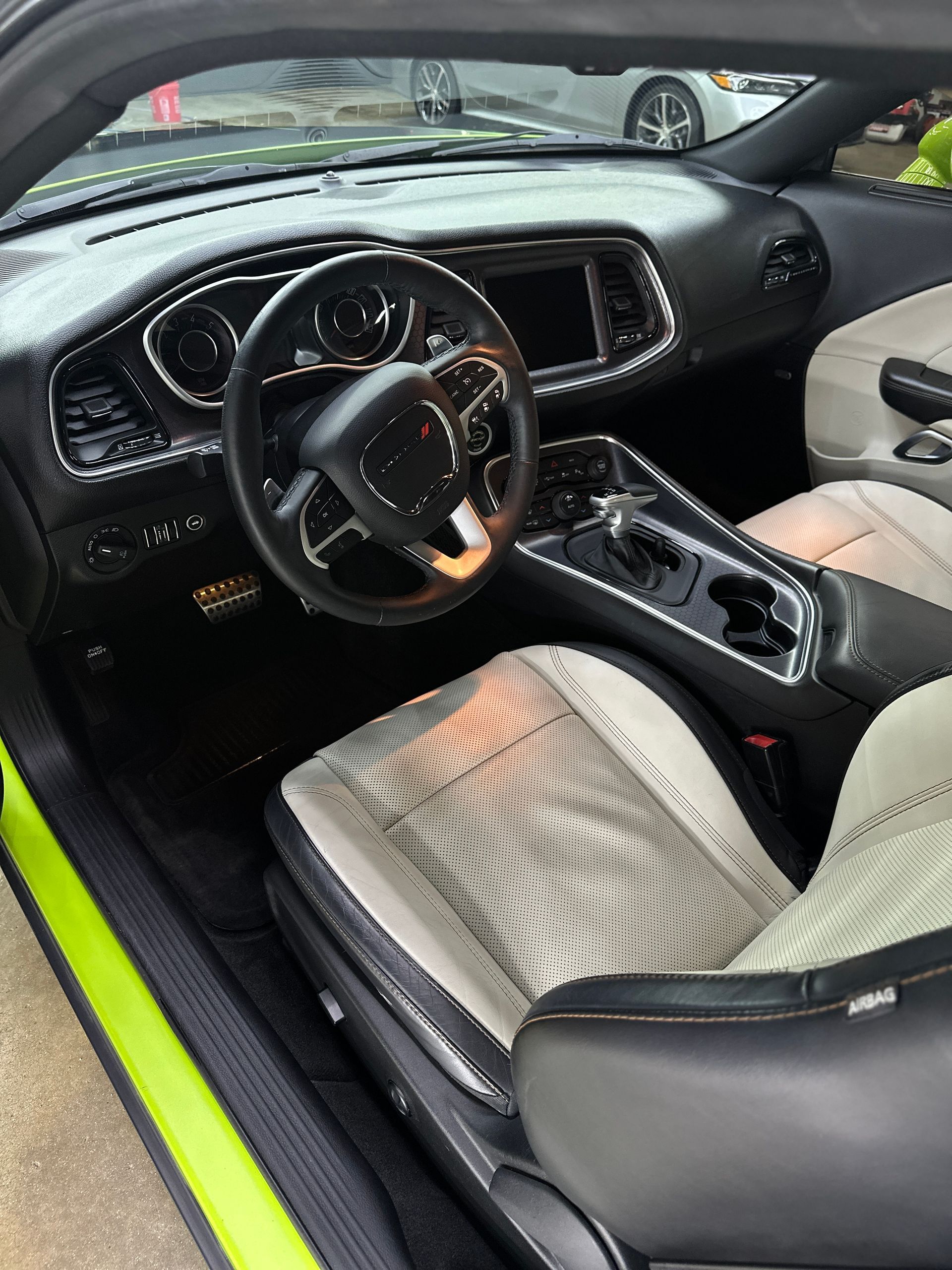 The driver's side interior of a modern car featuring a steering wheel, dashboard, and black and white perforated seats.