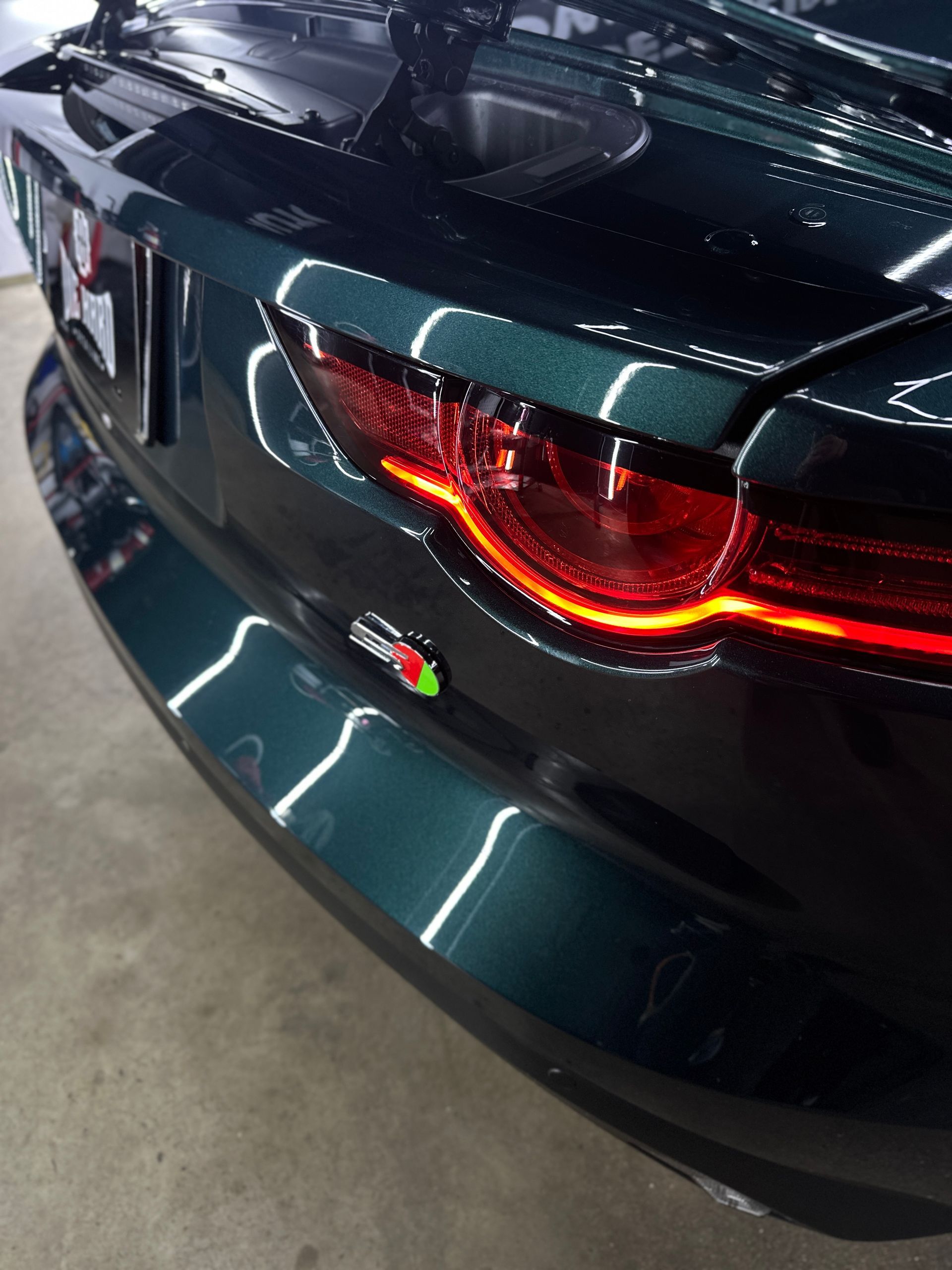 Rear view of a dark green Jaguar F-Type, highlighting the taillight and the Jaguar badge on the trunk lid.