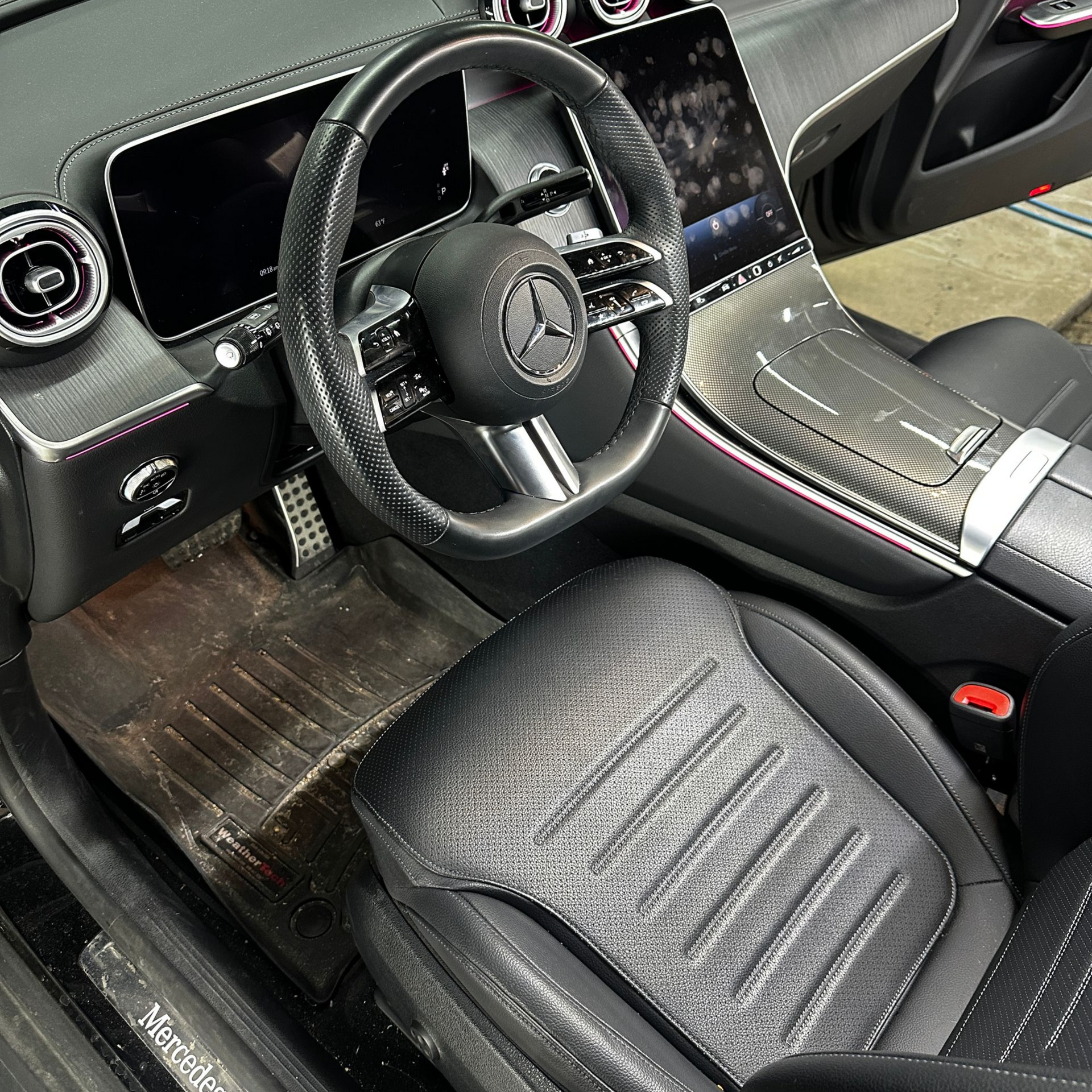 The driver’s side interior of a modern black Mercedes-Benz featuring a digital dashboard, steering wheel, and front seat.