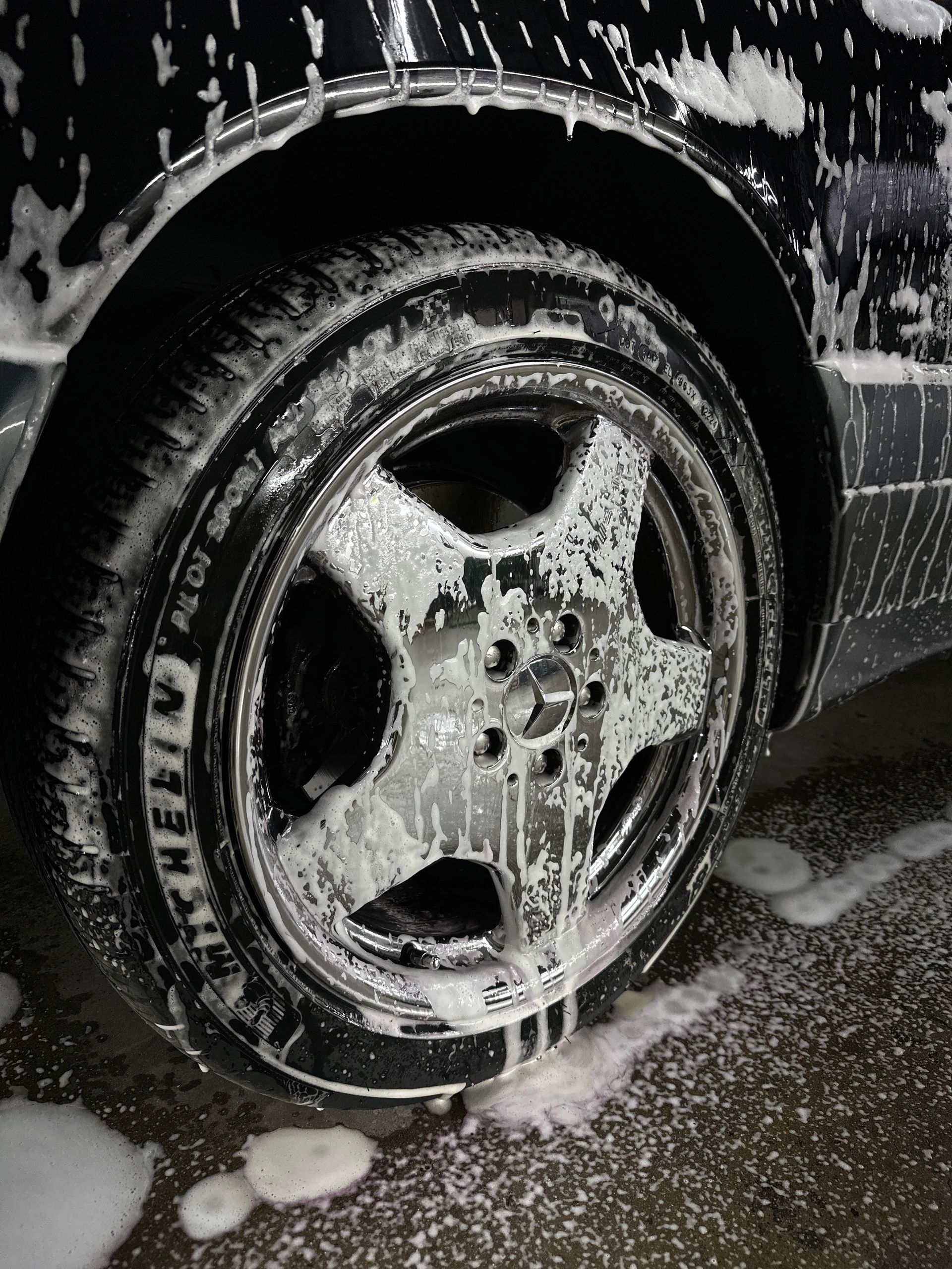 A close-up view of a car wheel covered in white soap suds during a car wash.