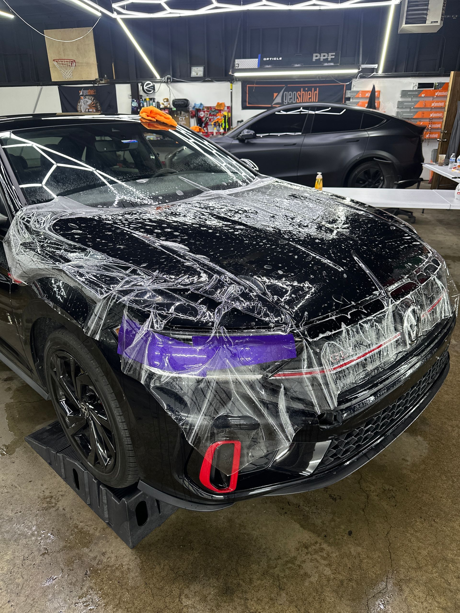A black car sits on service ramps in a garage, covered in soapy, sudsy water for a detailing wash.