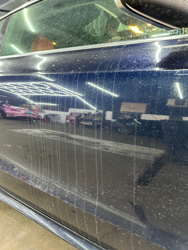 A dark blue car door with vertical streaks of dried water spots and grime on its exterior.