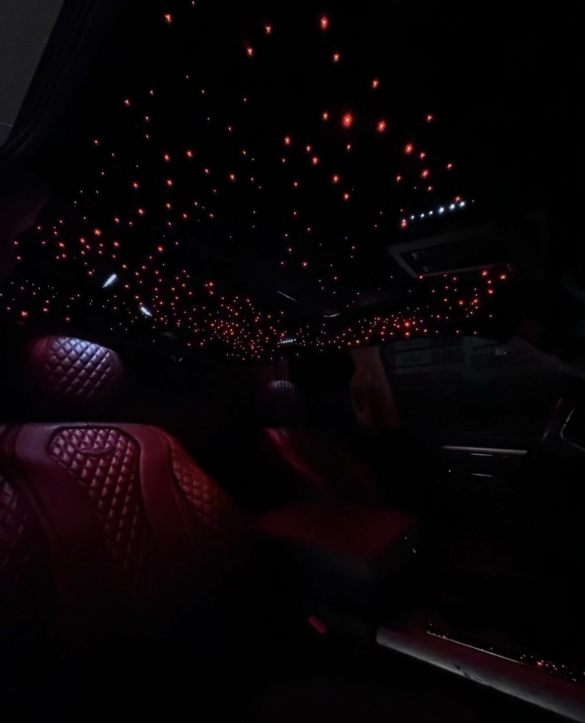 The interior of a vehicle featuring red leather diamond-stitched seats and a starlight headliner with glowing red lights.