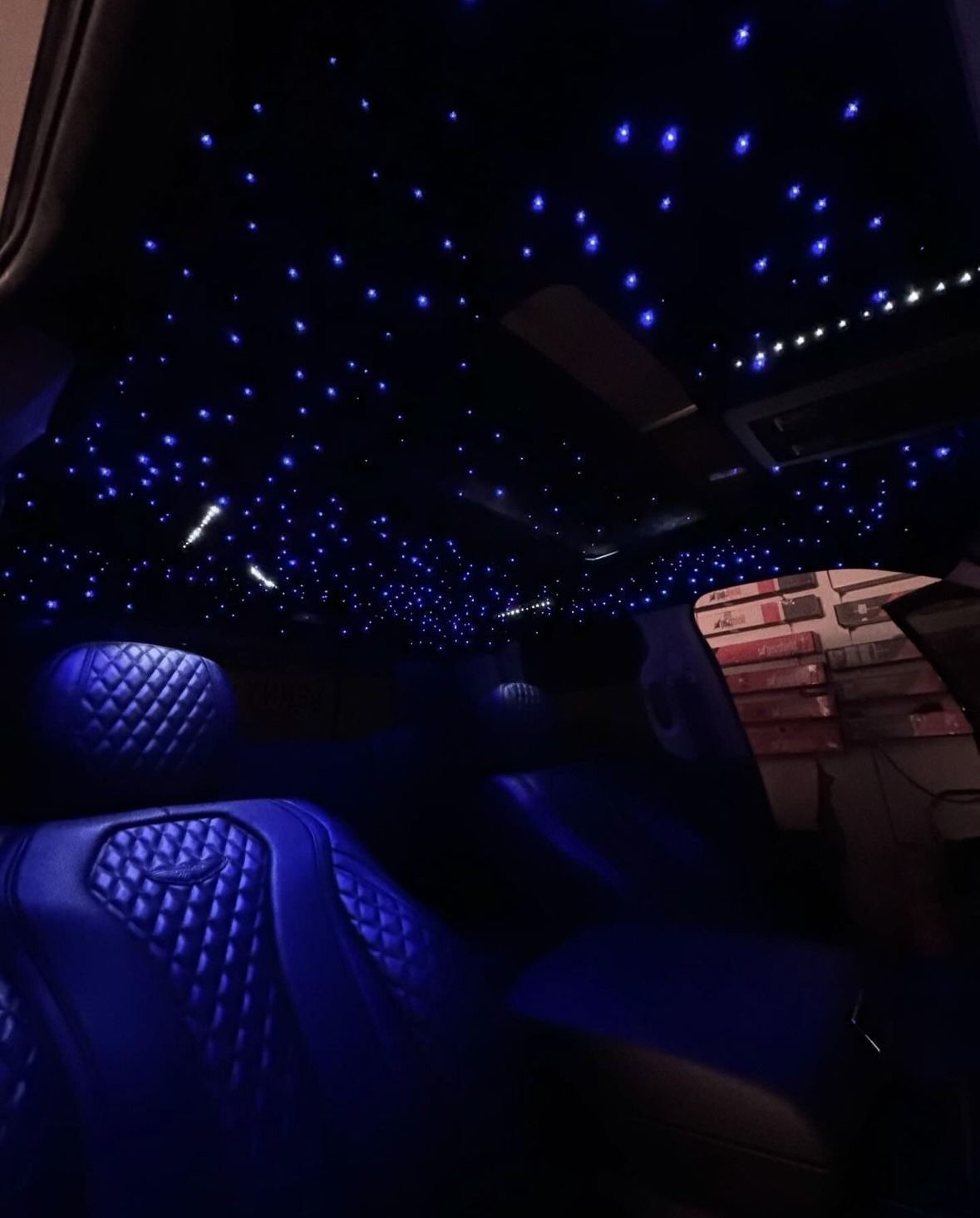 The interior of a vehicle featuring blue diamond-stitched leather seats and a starry night effect on the ceiling.