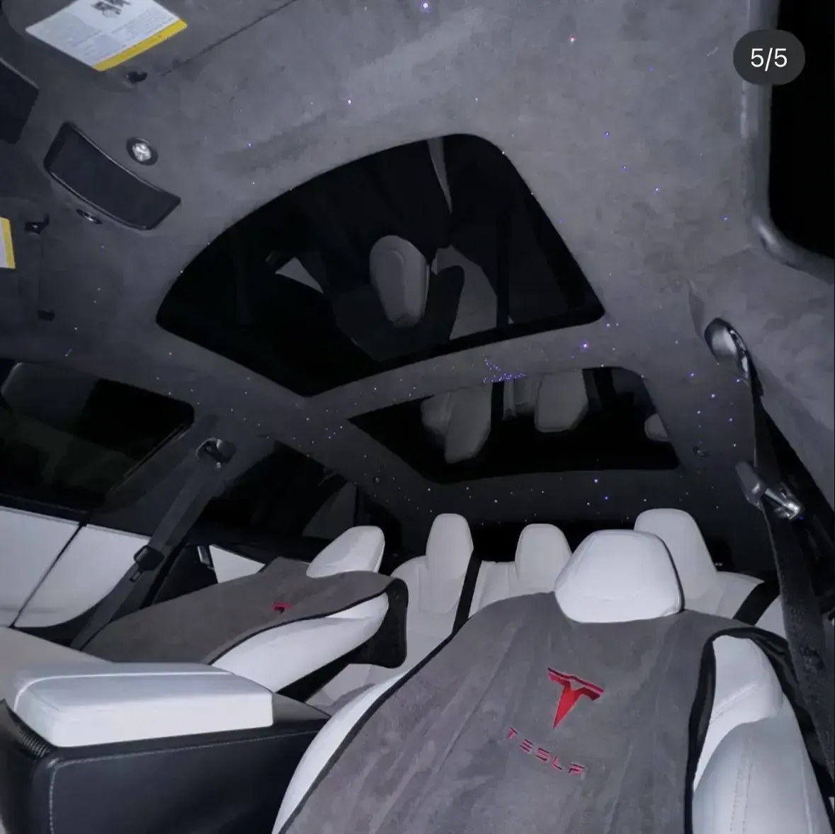 Interior of a car with white seats, grey seat covers featuring a red Tesla logo, and a starlit headliner.