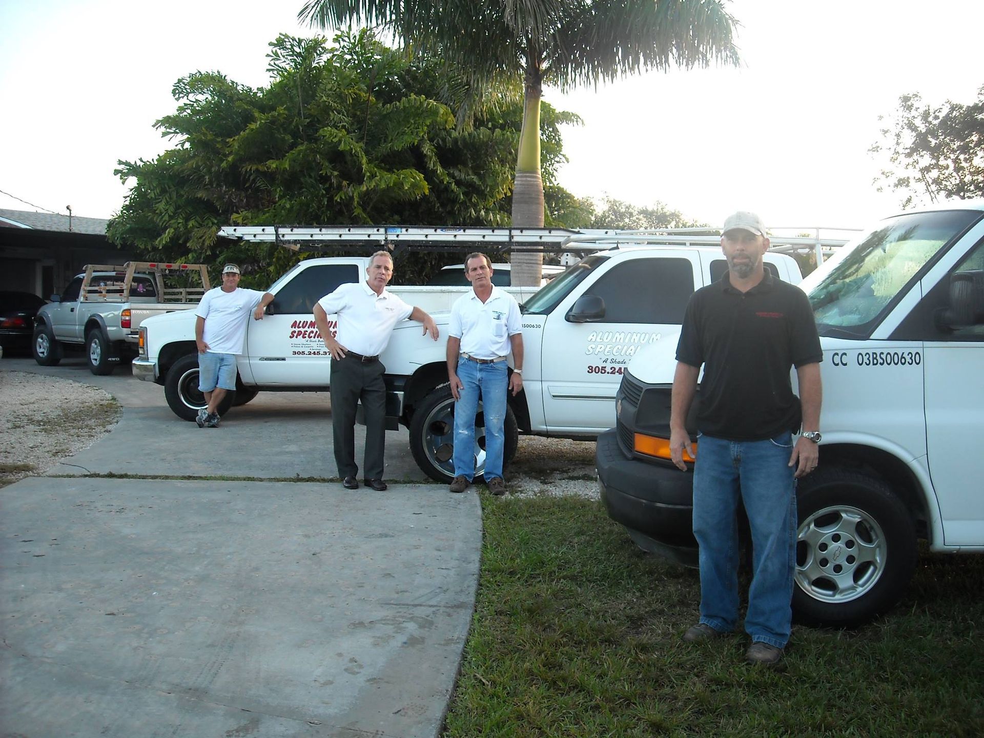 Four men standing by white vans in a parking lot near trees at sunset