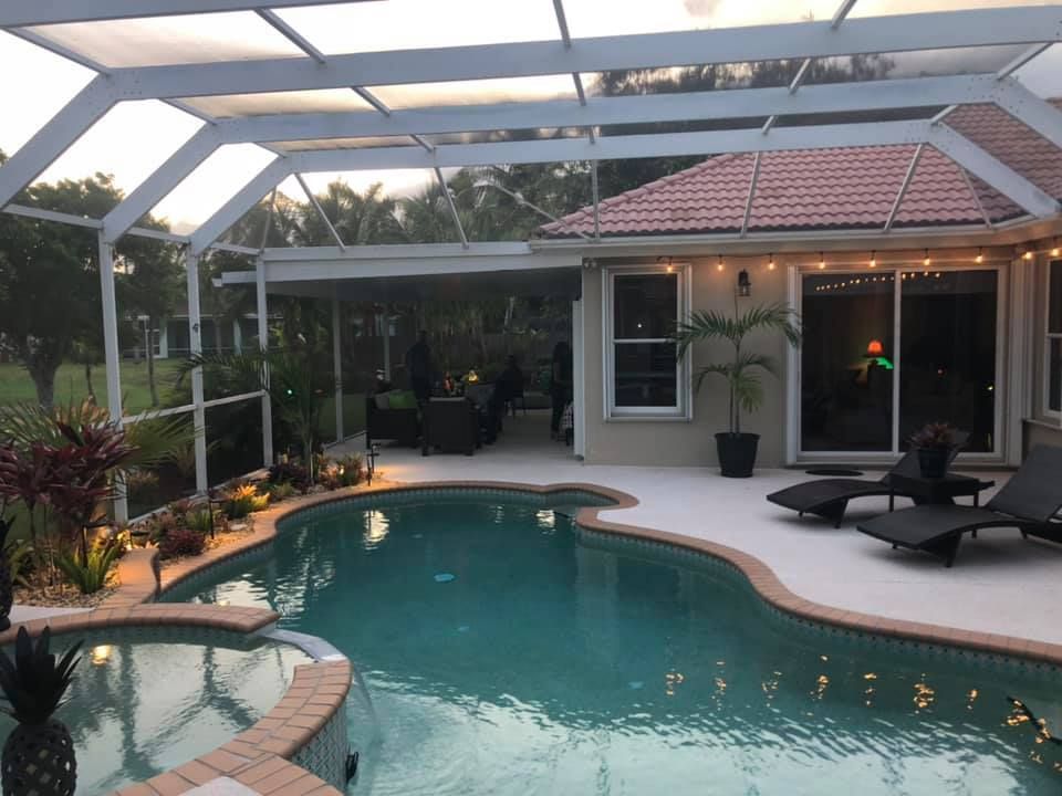 Backyard pool patio at dusk with lounge chairs and a screened lanai under a white pergola