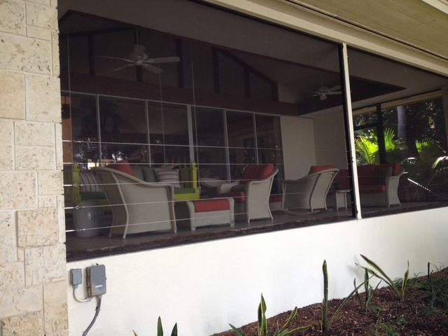 A house with a screened in porch and a grill in the backyard.