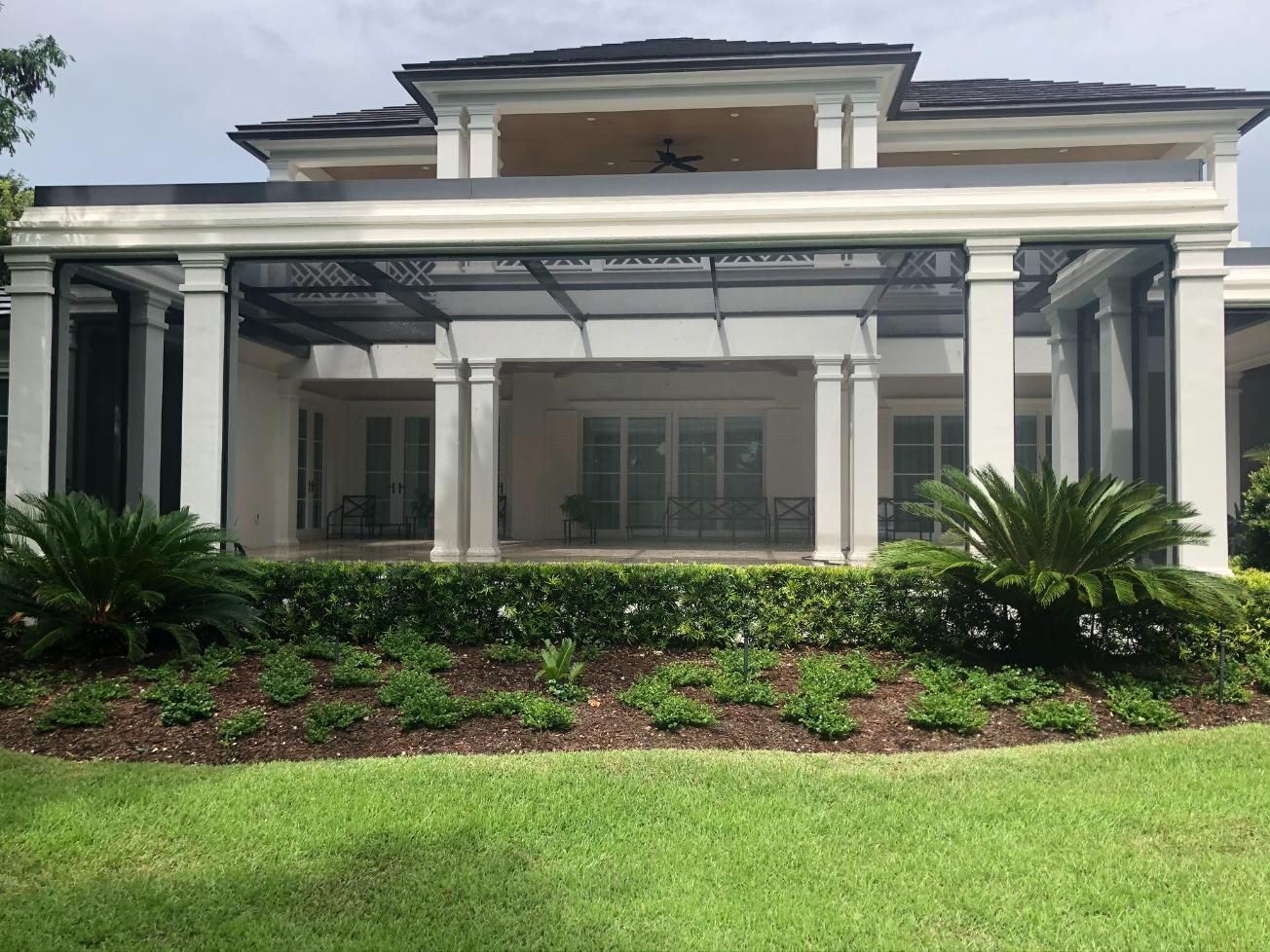 A large white house with a screened-in porch and a large lawn in front of it.