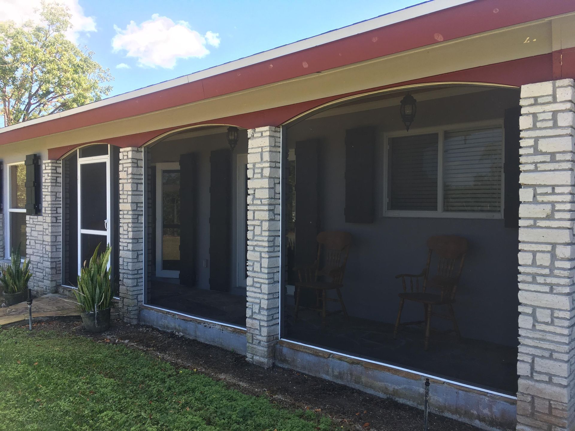 Front porch of a stone house with red roof, screened windows, and grass in front