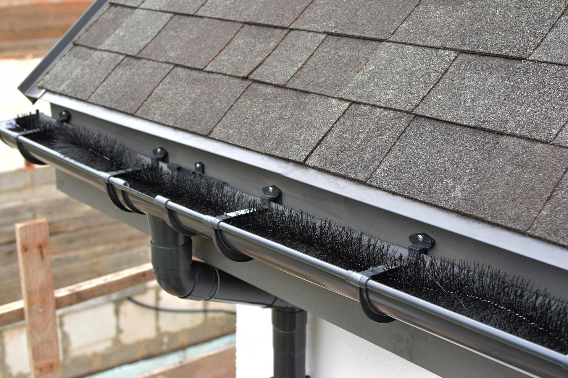 Black rain gutter with ice buildup under a shingled roof