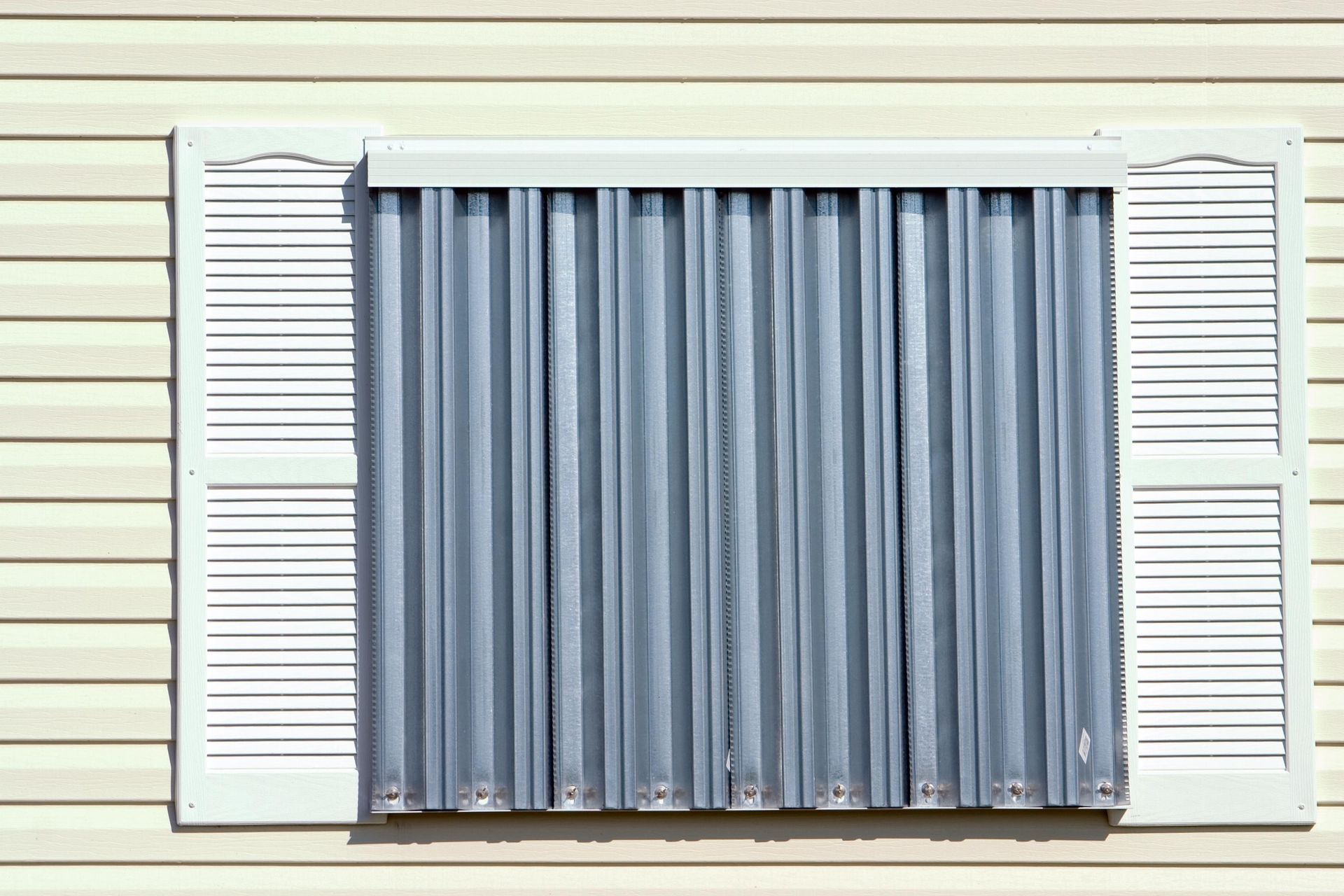 Window with white shutters and blue curtains on a beige house exterior