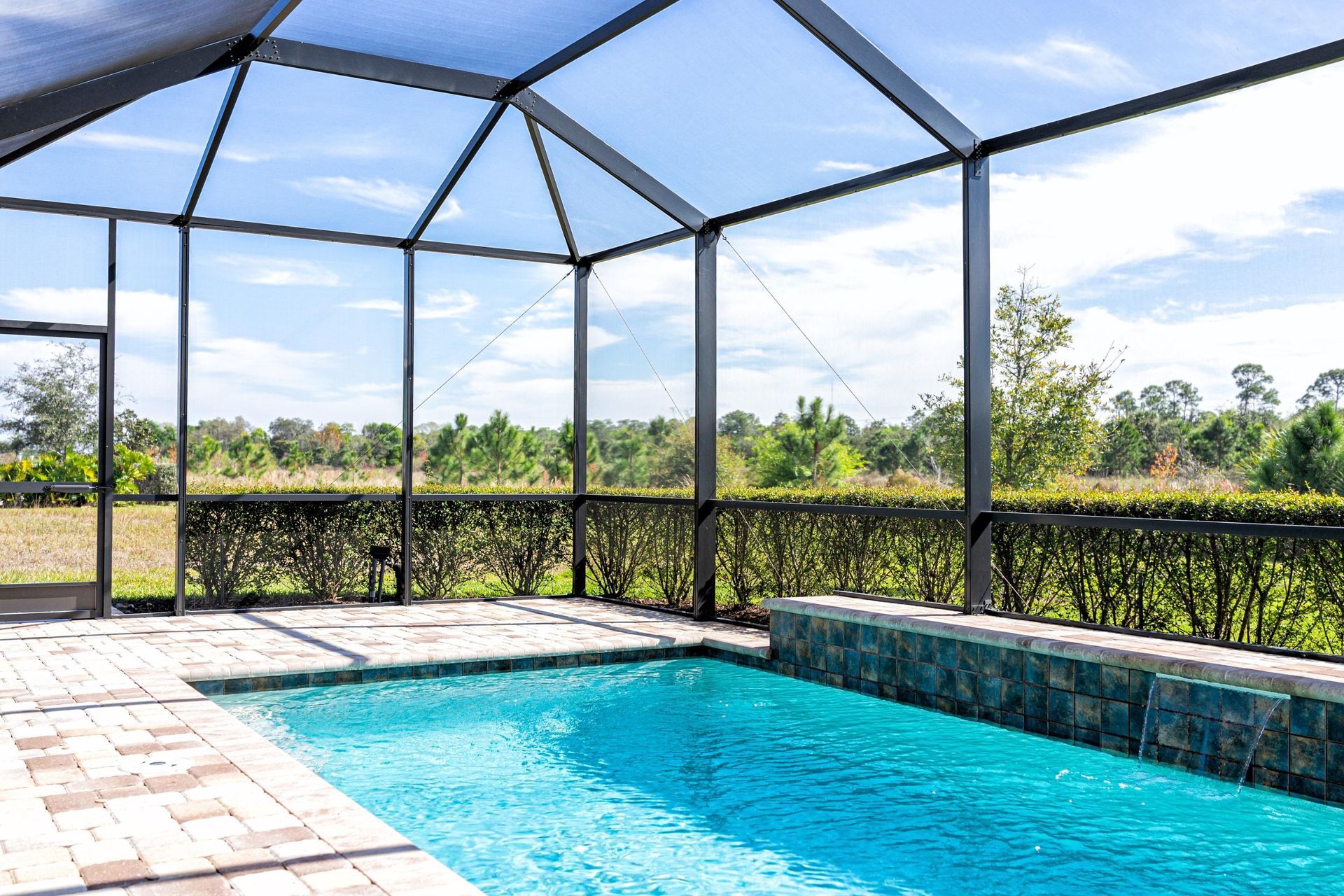 Screened outdoor pool with turquoise water beside a stone ledge and patio under a black-framed enclosure