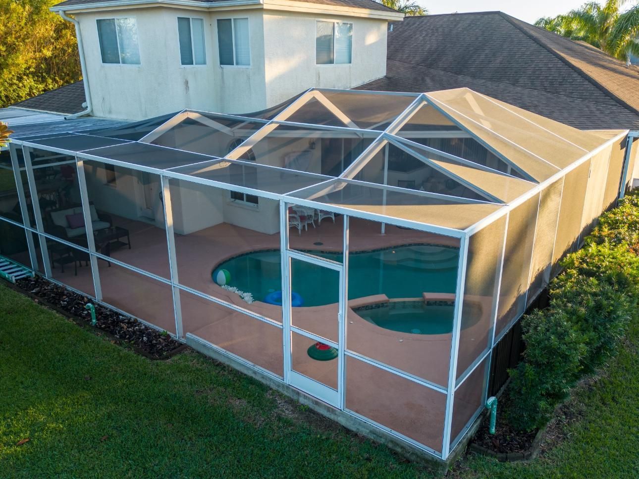 Screened backyard pool enclosure beside a two-story house with a covered patio and green lawn