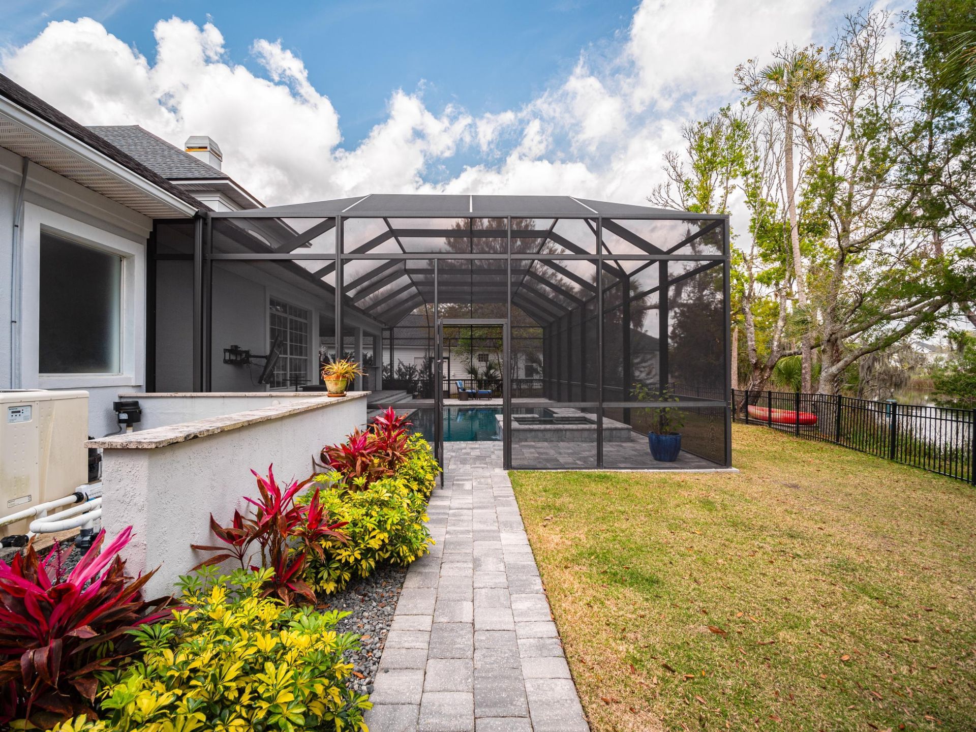 Backyard patio with screened enclosure, stone path, and colorful plants beside a lawn